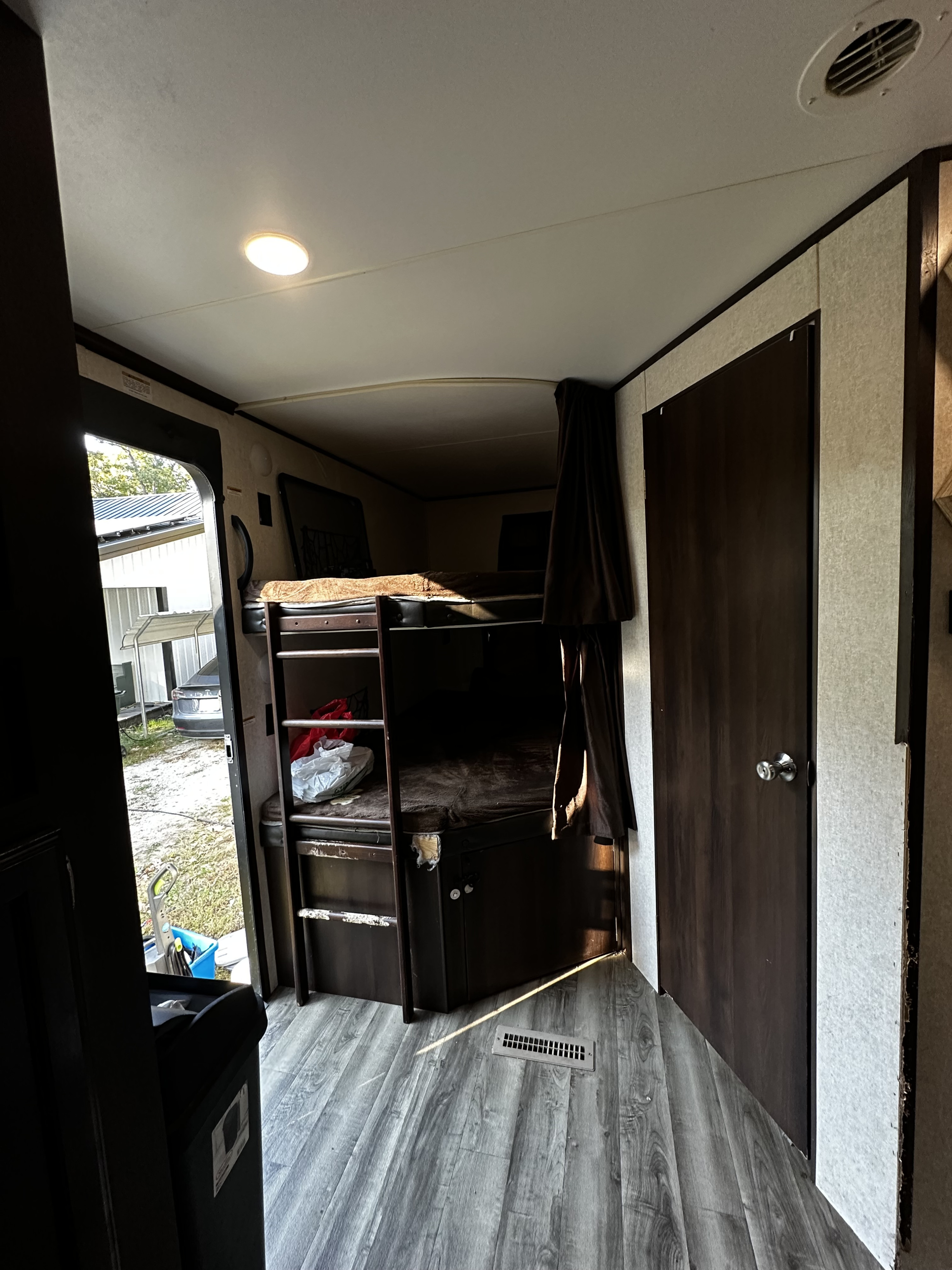 Inside an RV rental, showing a bunk bed area with dark wood details, light floor, and the main door open to outside.. Jayco Jay Flight 2019