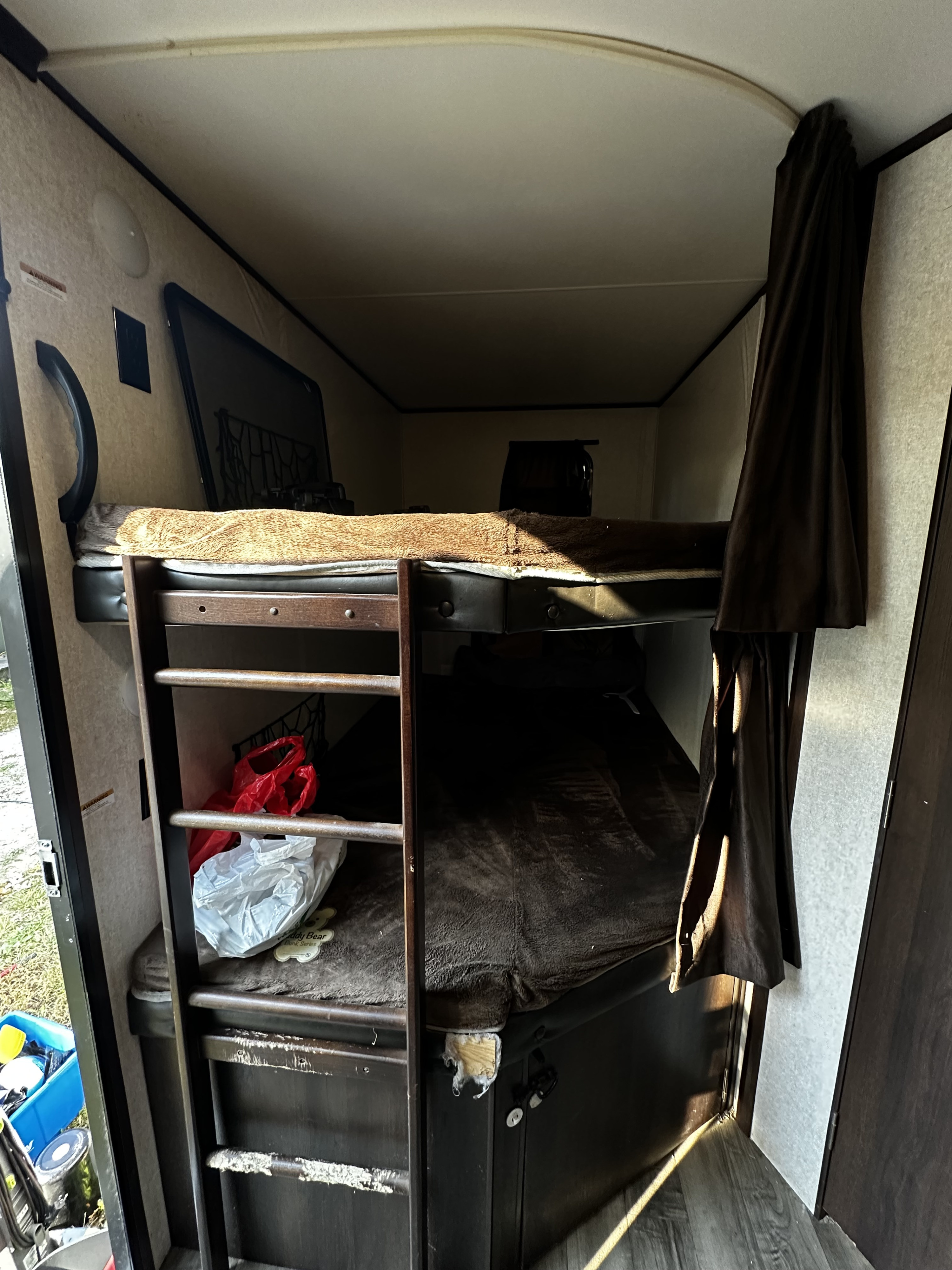 Interior of an RV rental: stacked bunk beds with a ladder, blankets, and stored belongings, lit by daylight.. Jayco Jay Flight 2019