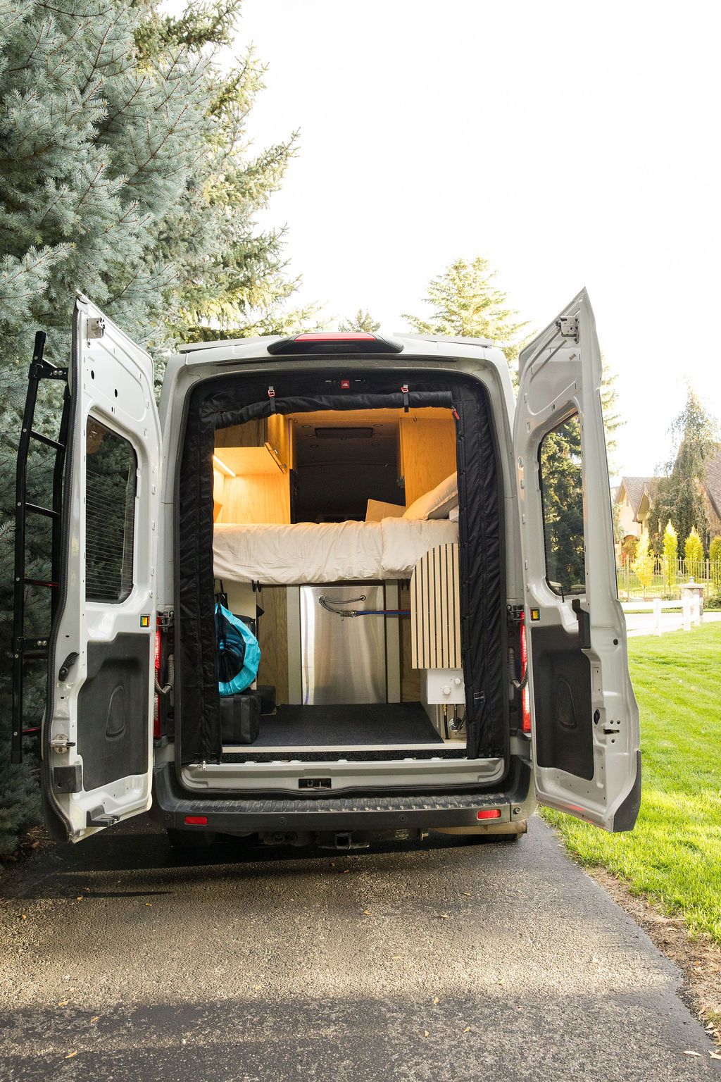 See inside this white custom camper van RV rental, showcasing its cozy bed, wood interior, and smart storage ready for adventure.. Ford Transit 2022