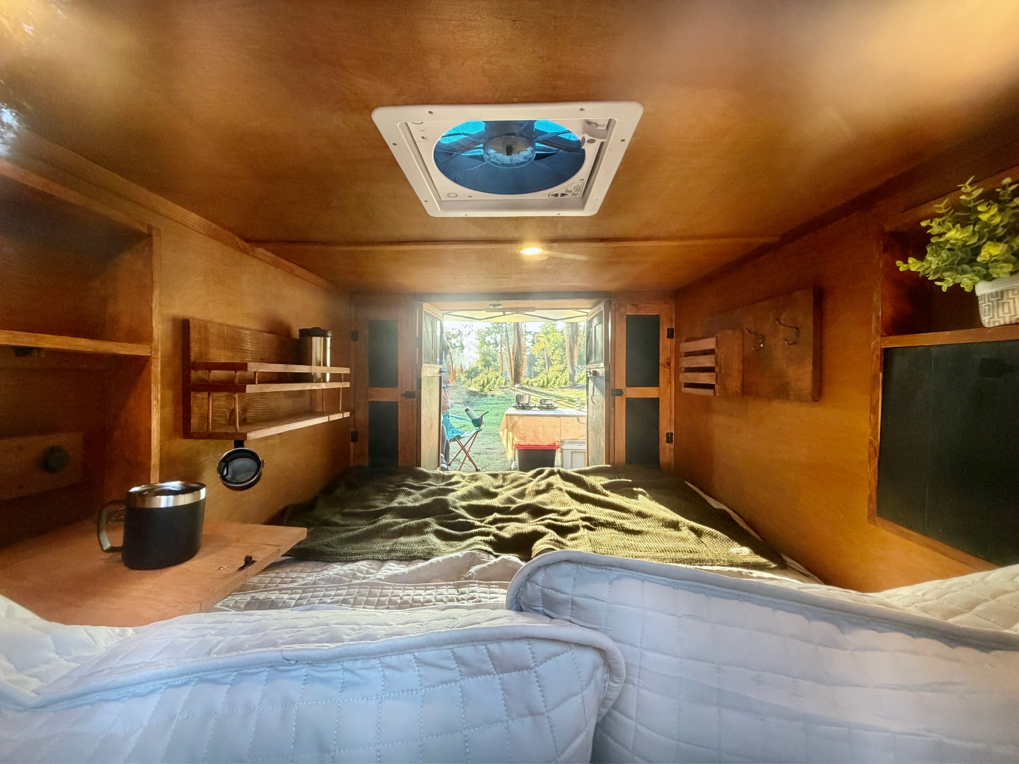 Cozy RV rental interior: wooden walls, comfy bed, and open view to a beautiful outdoor campsite.. custom CHANG 2011