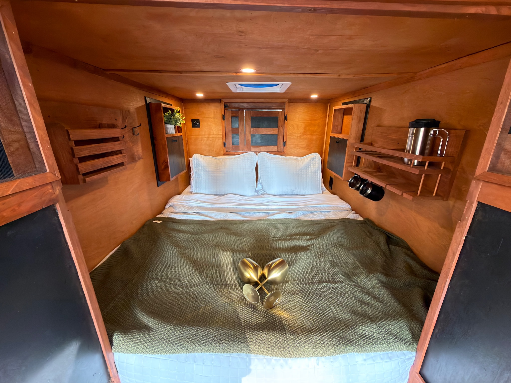 This glamping RV rental offers a cozy wood-paneled bedroom with a bed, golden glasses, and practical built-in storage.. custom CHANG 2011