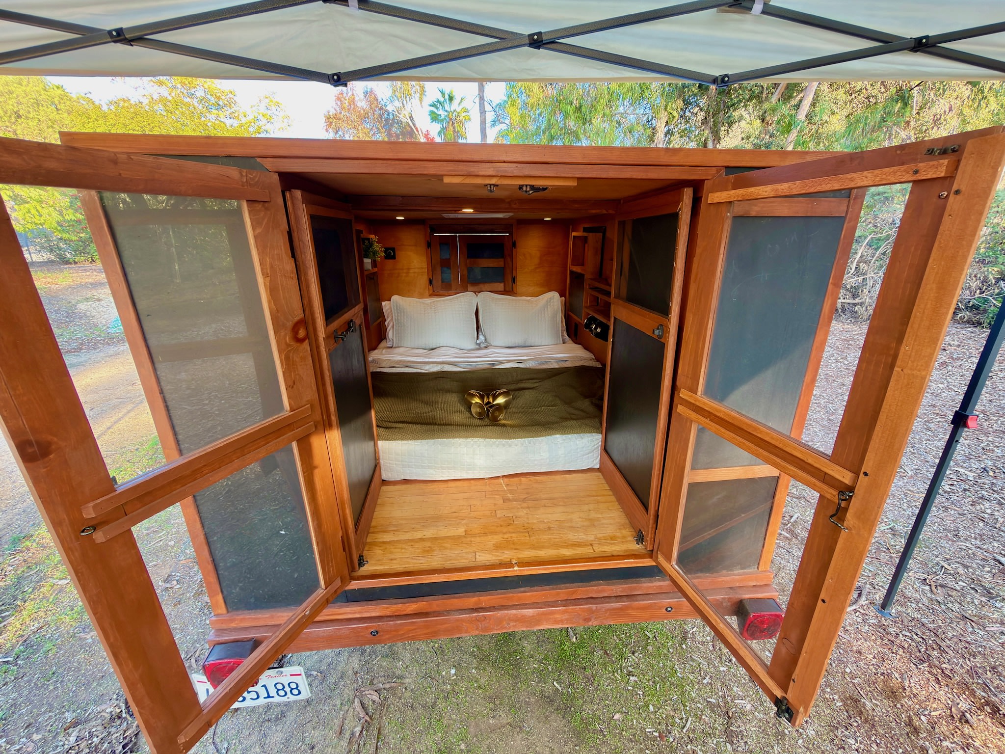 Cozy RV rental: inside a wooden camper with open doors, revealing a comfy bed and built-in storage. Perfect for glamping adventures.. custom CHANG 2011