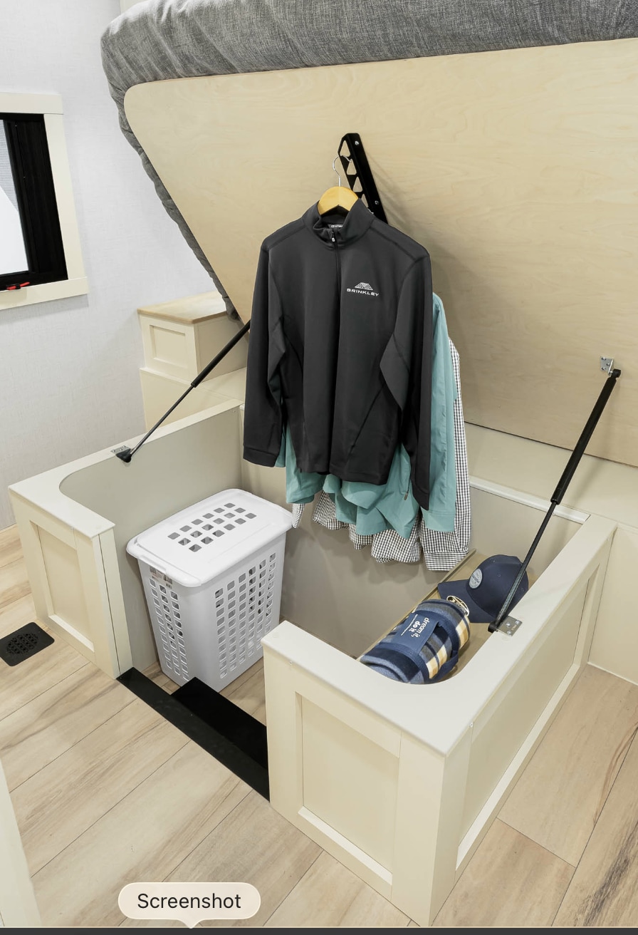RV rental bedroom: bed lifted to reveal spacious under-bed storage with hanging clothes, a laundry hamper, and cubbies.. Brinkley RV Model I 2025