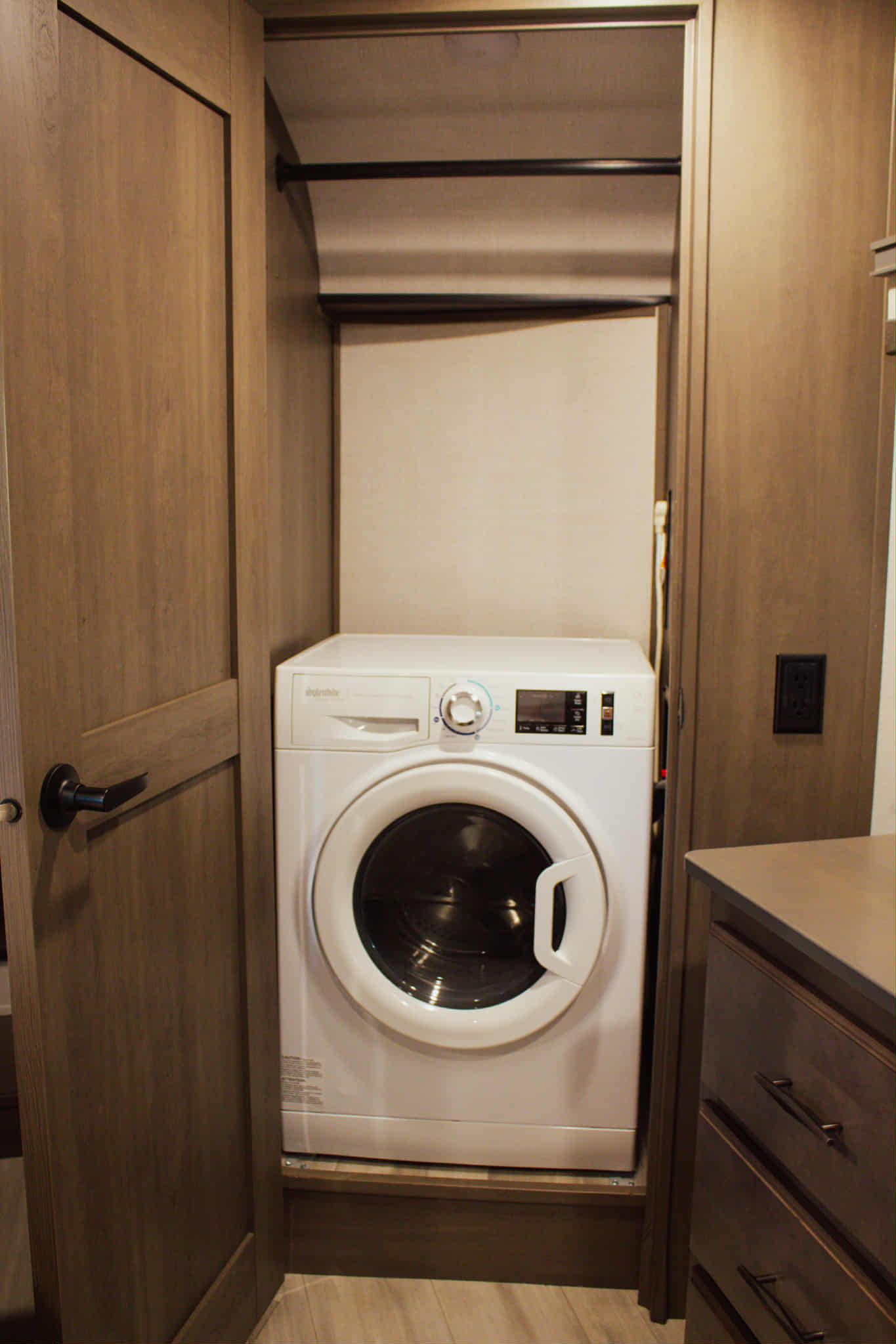 Compact front-load washing machine neatly tucked into a closet within an RV rental, with hanging rods overhead for laundry convenience.. Grand Design Solitude 2023