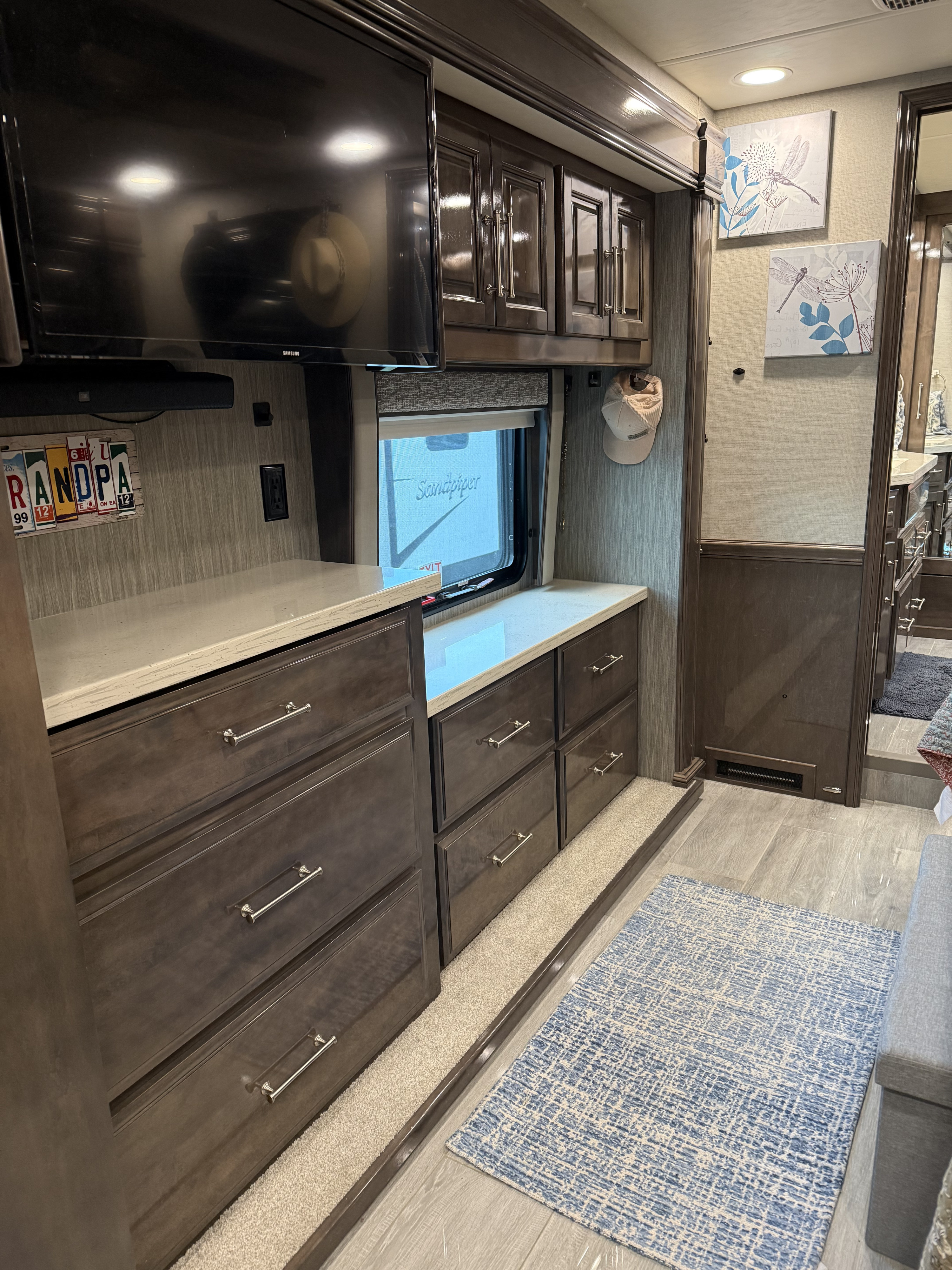 Modern RV rental interior with sleek dark wood cabinetry, a mounted TV, storage drawers, and light-toned decor.. Entegra Coach Aspire 2021