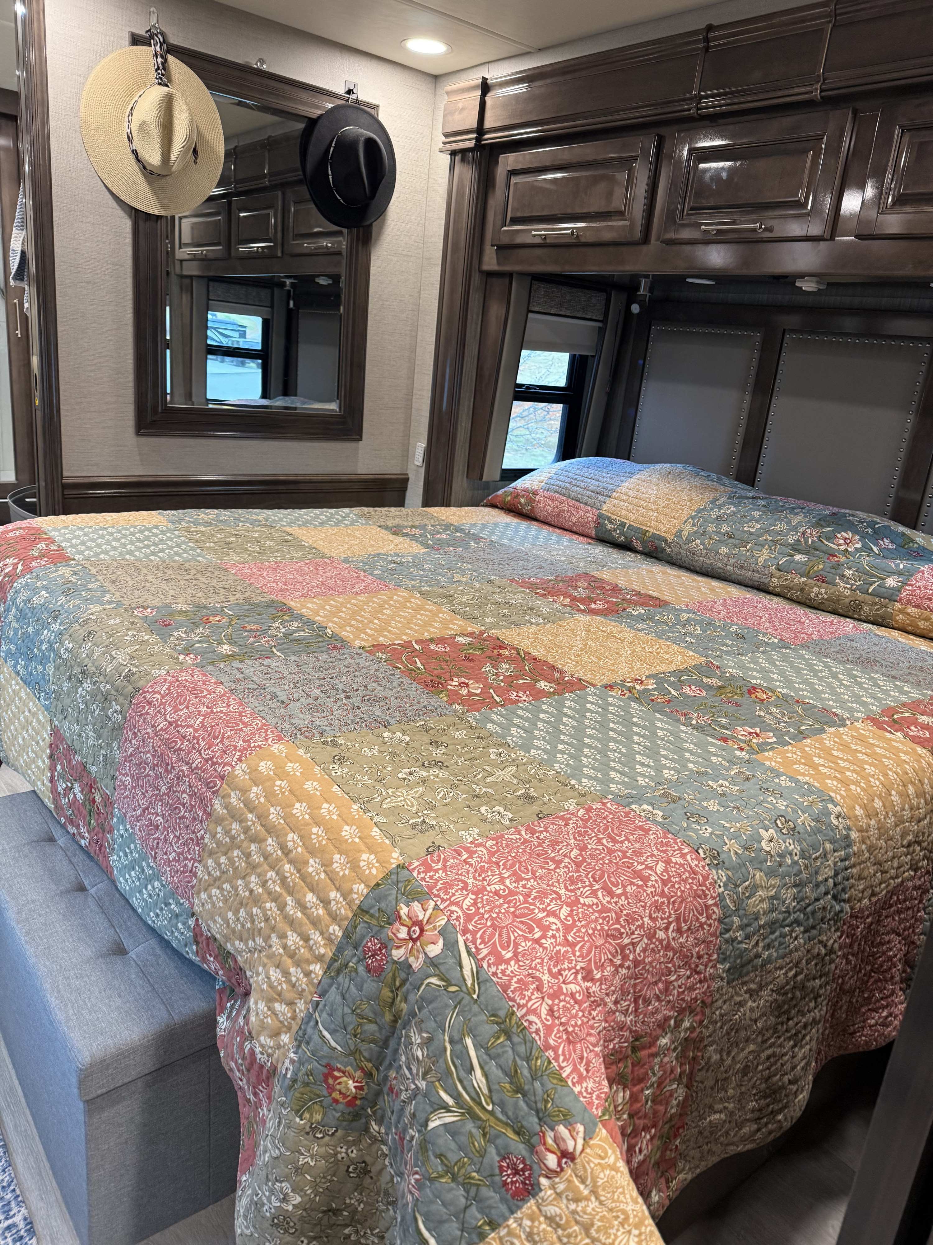 Cozy RV rental bedroom with a colorful patchwork quilt, dark wood cabinets, and padded headboard for comfortable travel.. Entegra Coach Aspire 2021