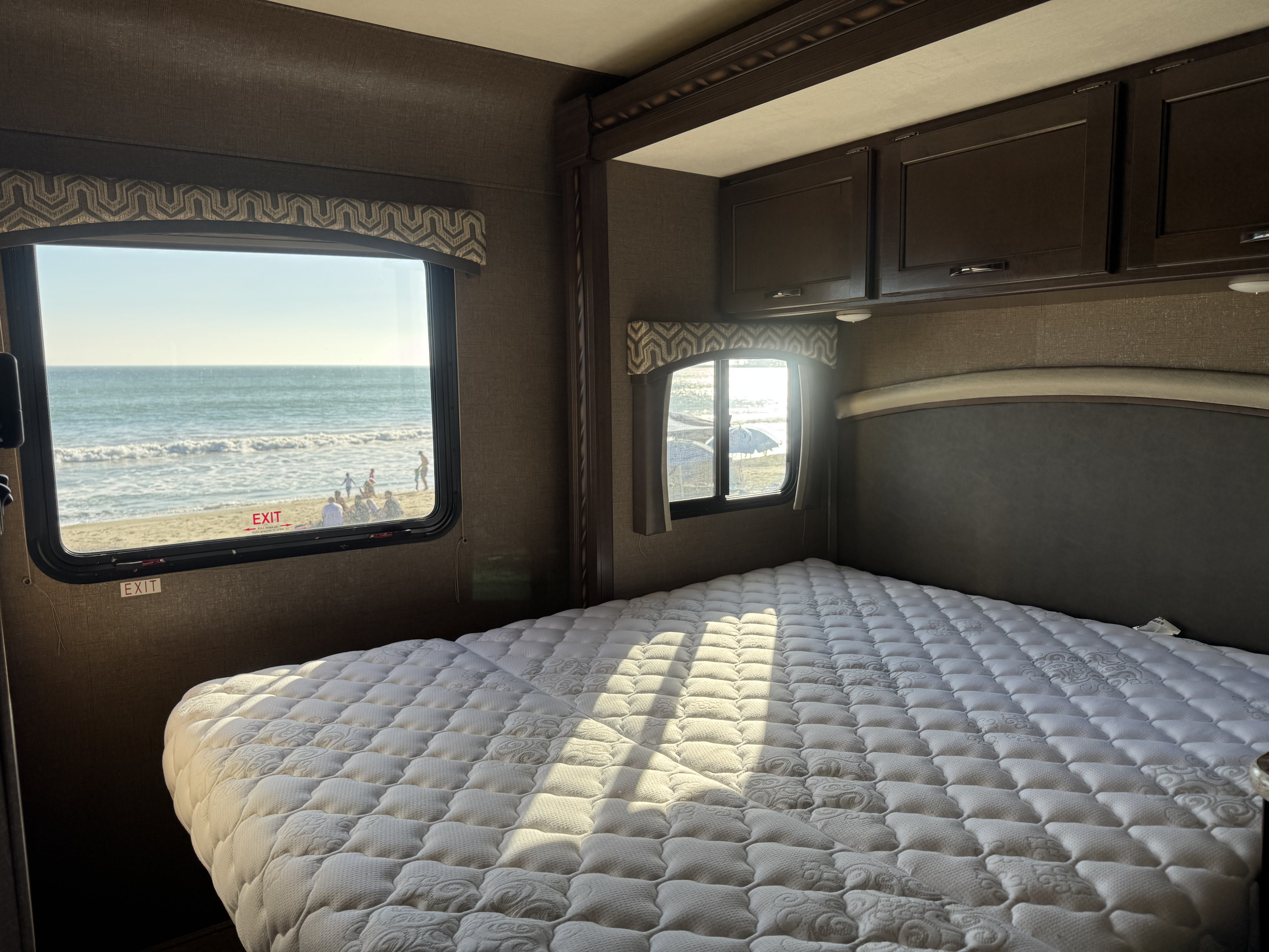 RV rental bedroom with a stunning ocean view, featuring a comfortable bed overlooking the beach and waves.. Thor Chateau 2019