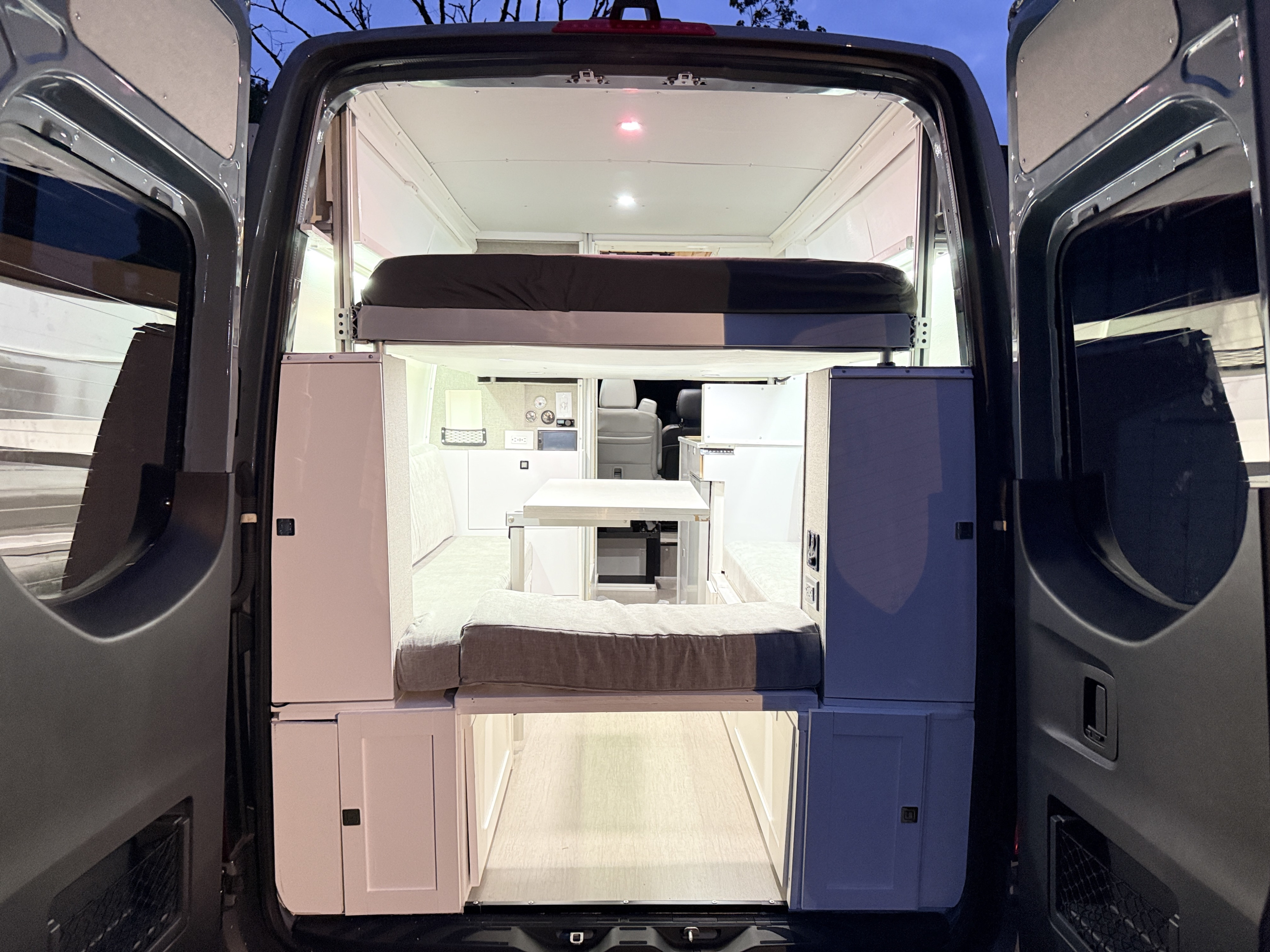 View of an RV rental camper van's interior from the open rear doors, revealing a cozy bed, dining area, and compact living space.. Mercedes-Benz Sprinter 2500 4x4 2021