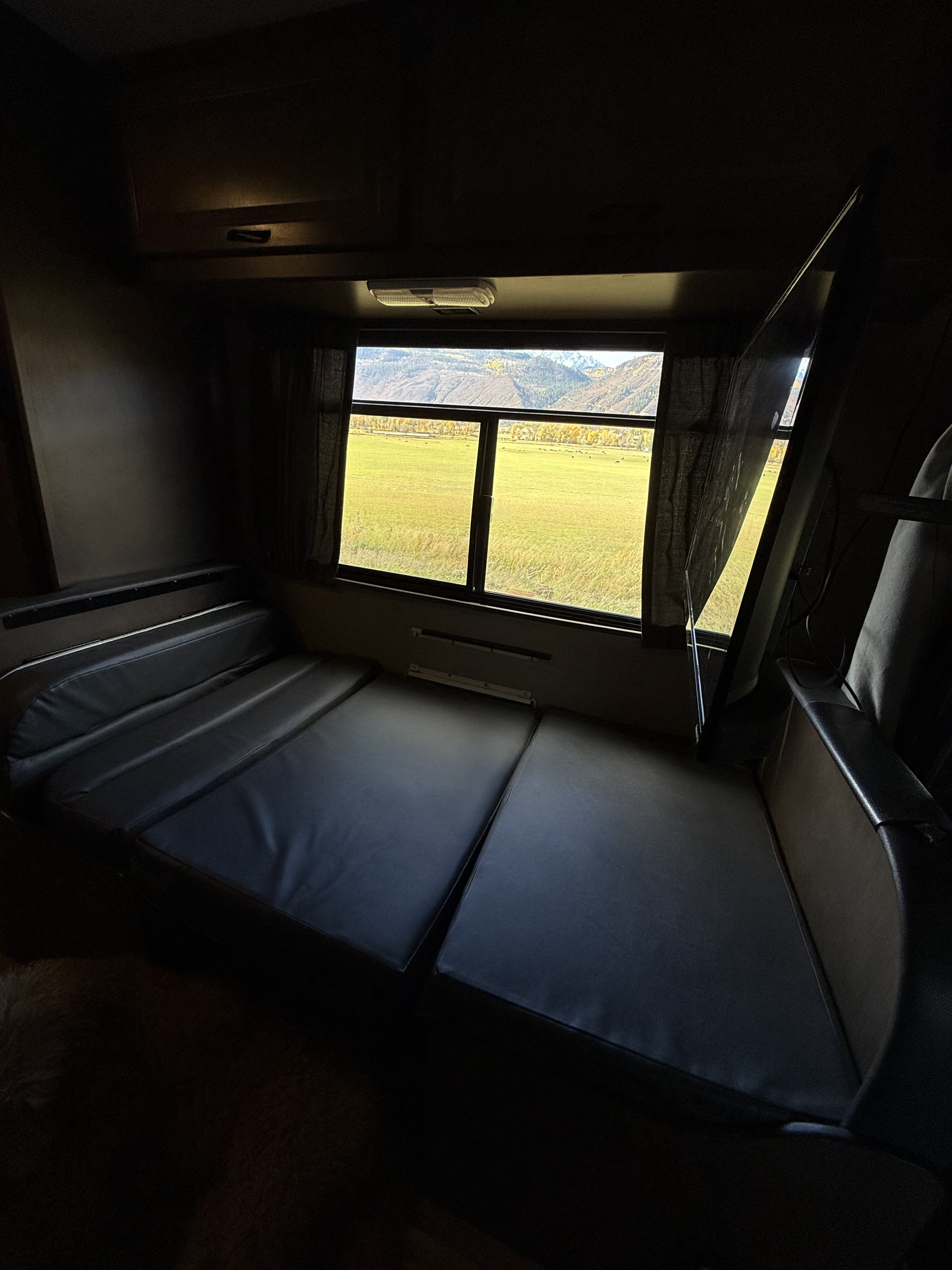 RV rental interior featuring a convertible couch-bed, TV, and a scenic window view of autumn mountains and a green field.. Thor Majestic 2019