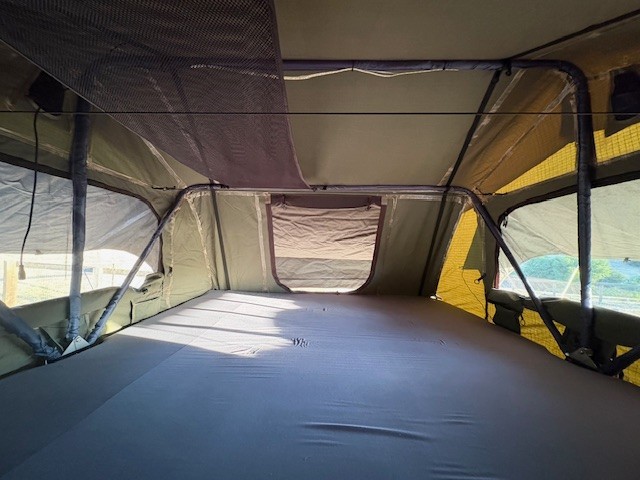 Inside an rv rental rooftop tent: a cozy sleeping area. Features mattress, screen windows, & storage net for camping.. Runaway Trailers The Range Runner 2024