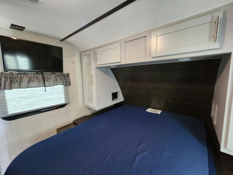 Inside this RV rental bedroom: a comfy blue bed, mounted TV, window with blinds, and white overhead cabinets.. Keystone RV Bullet Ultra Lite 2019