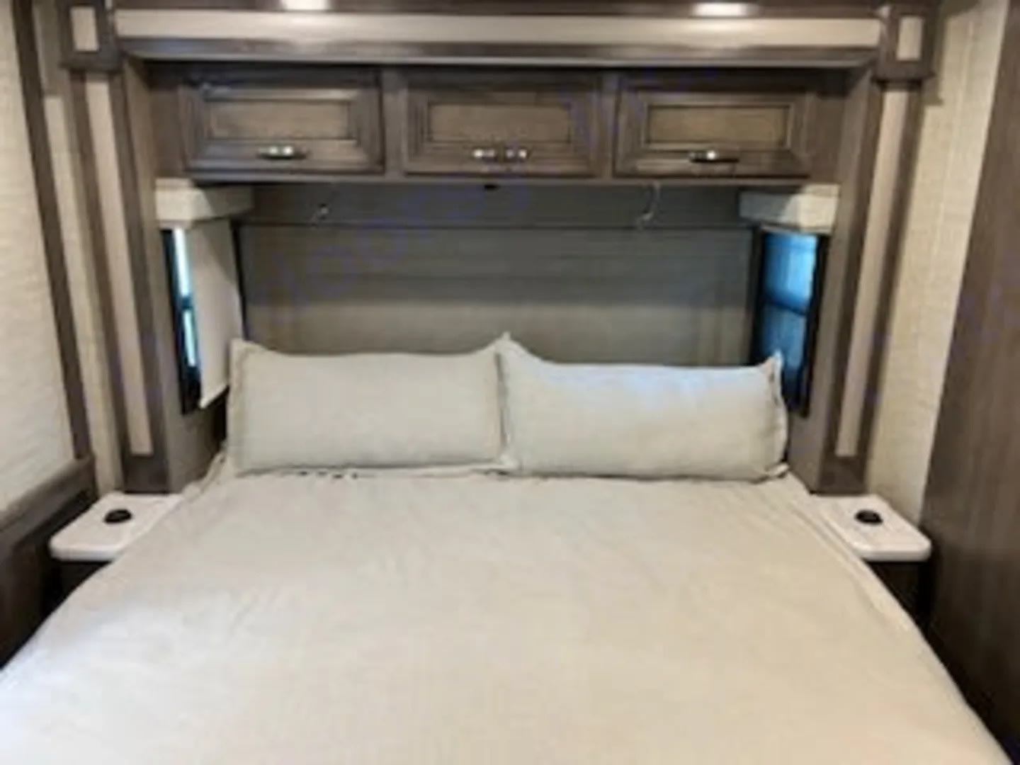 RV rental bedroom with a made-up bed, overhead storage, side windows, and small nightstands. Comfortable travel awaits.. Entegra Coach Vision XL 2023
