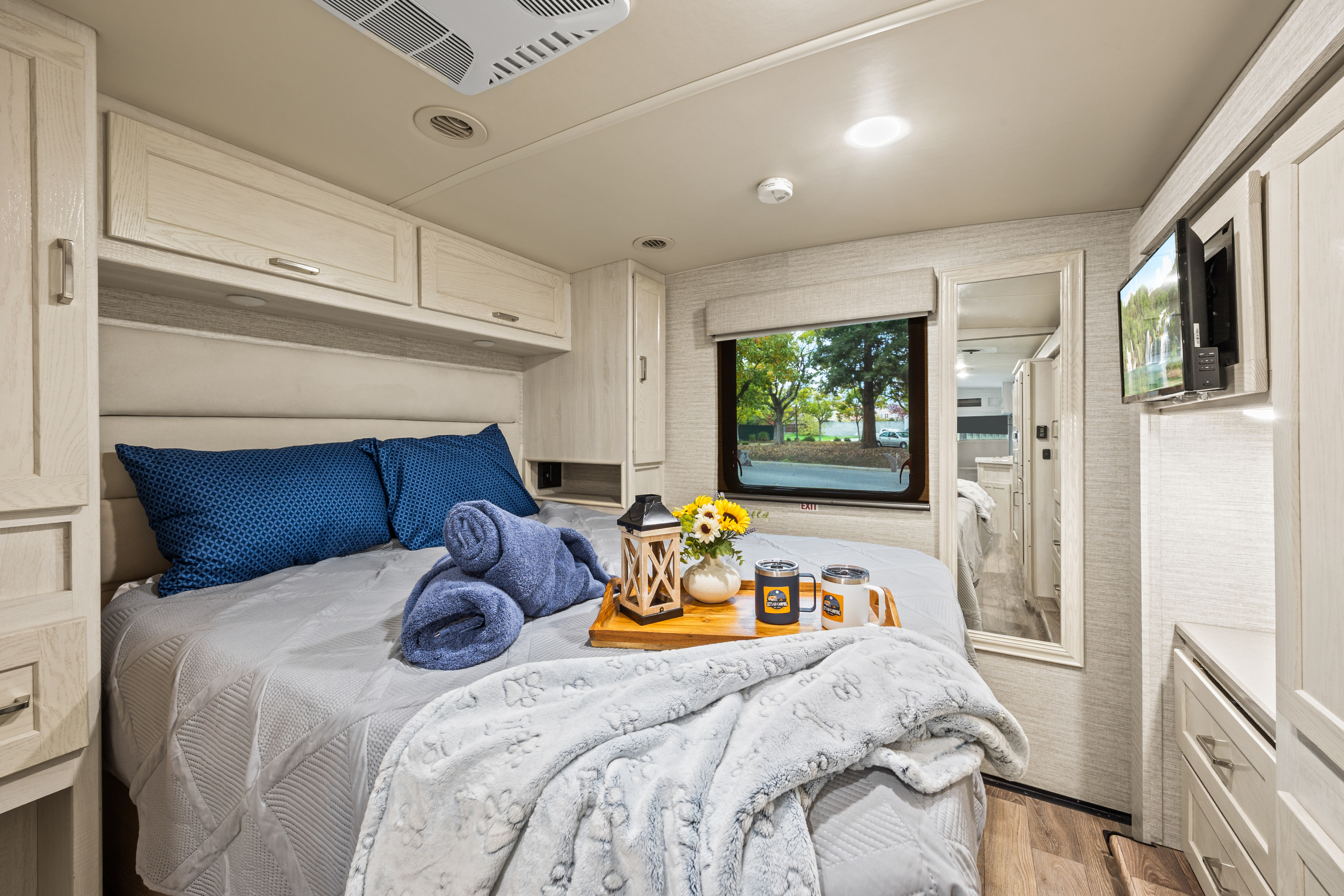 Cozy RV rental bedroom with a comfortable bed, overhead storage, TV, and a window view. Relax and enjoy your adventure!. Winnebago Adventure 2020