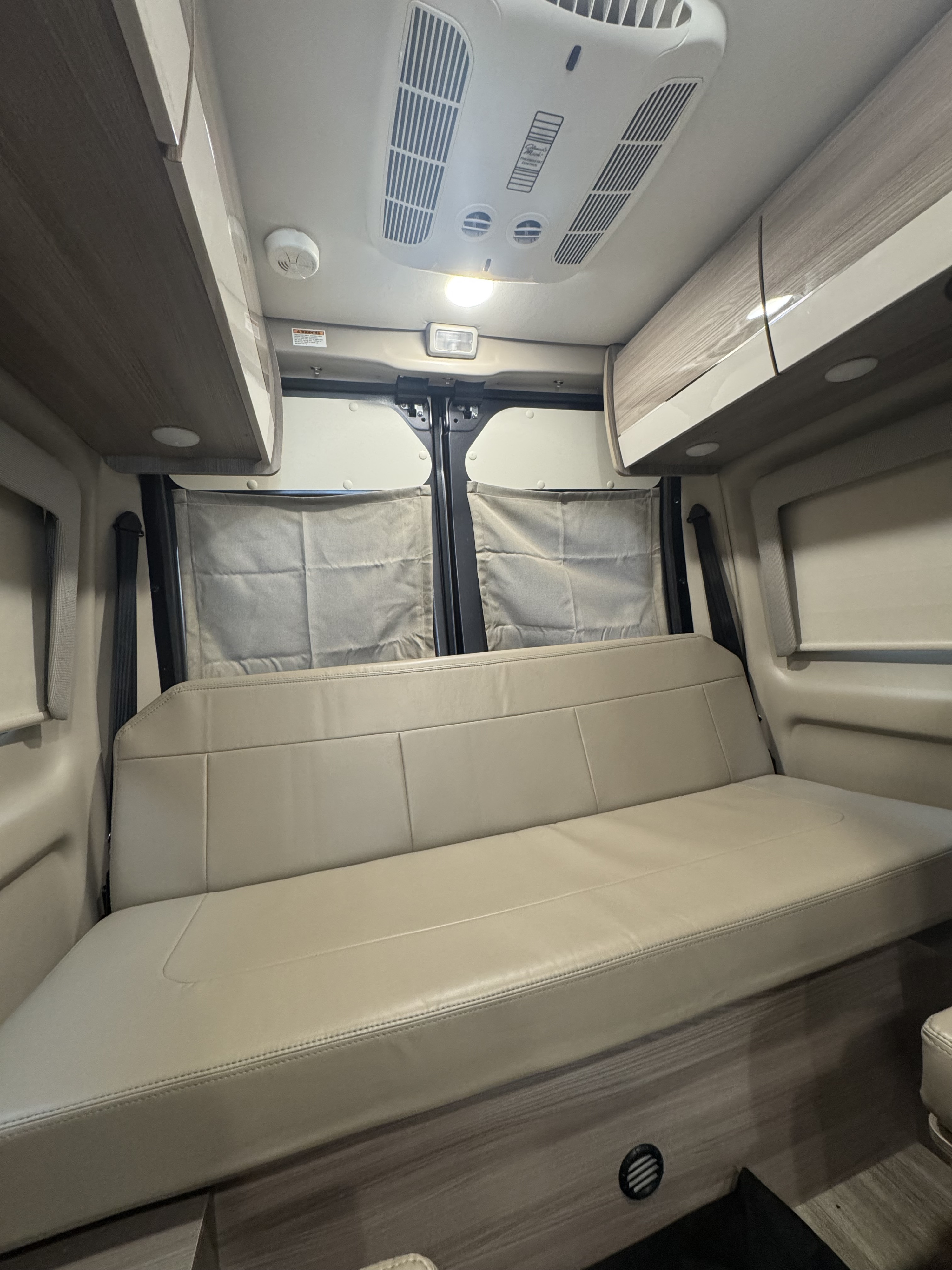 Spacious RV rental interior featuring a comfortable light-colored bench seat/bed, overhead cabinets, and ceiling AC unit.. Thor Sequence 2024