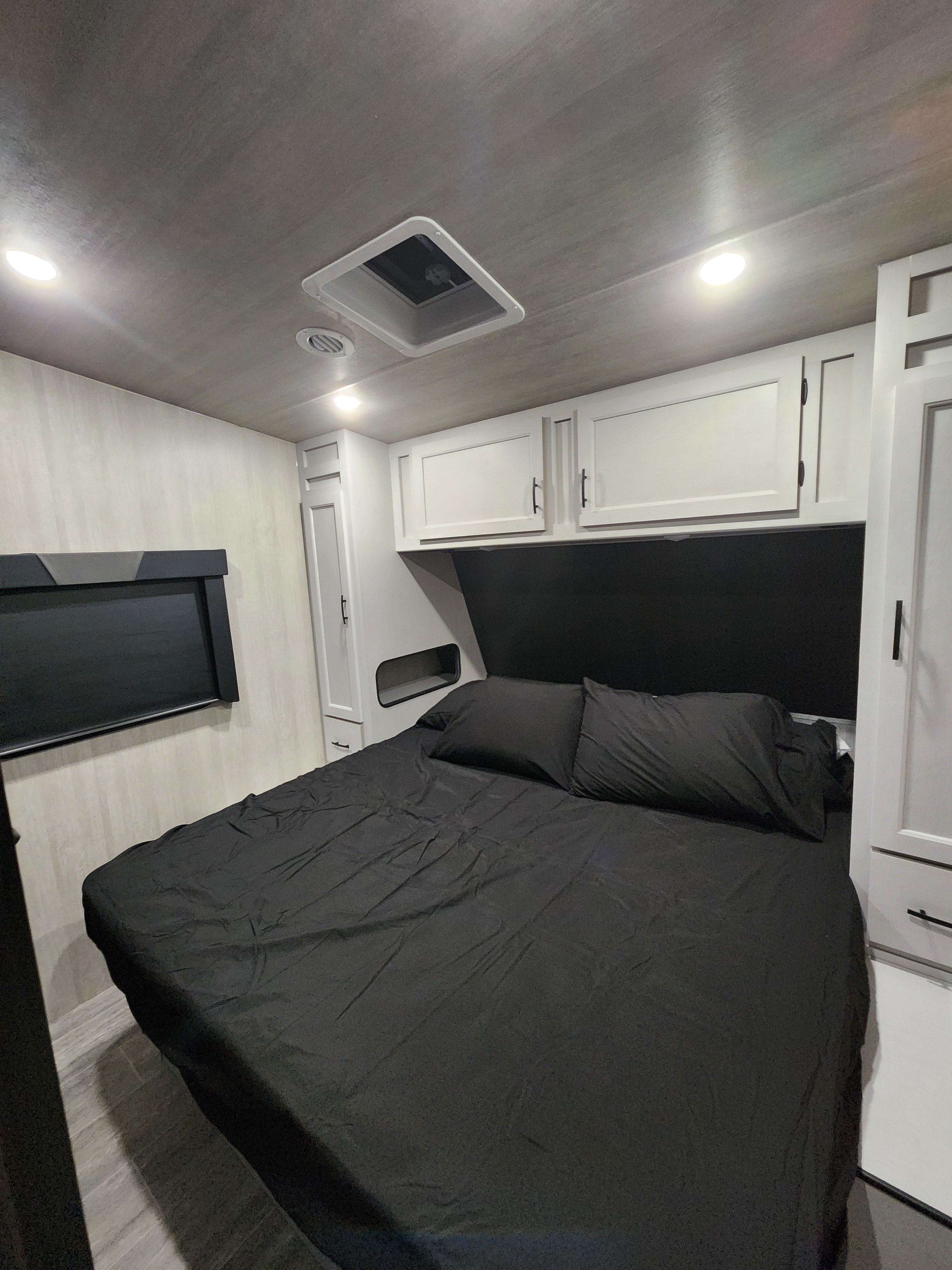 RV rental bedroom with modern black and white decor. Features a bed, overhead cabinets, and bright lighting for a comfortable stay.. Genesis Supreme Rv Genesis Supreme 2026