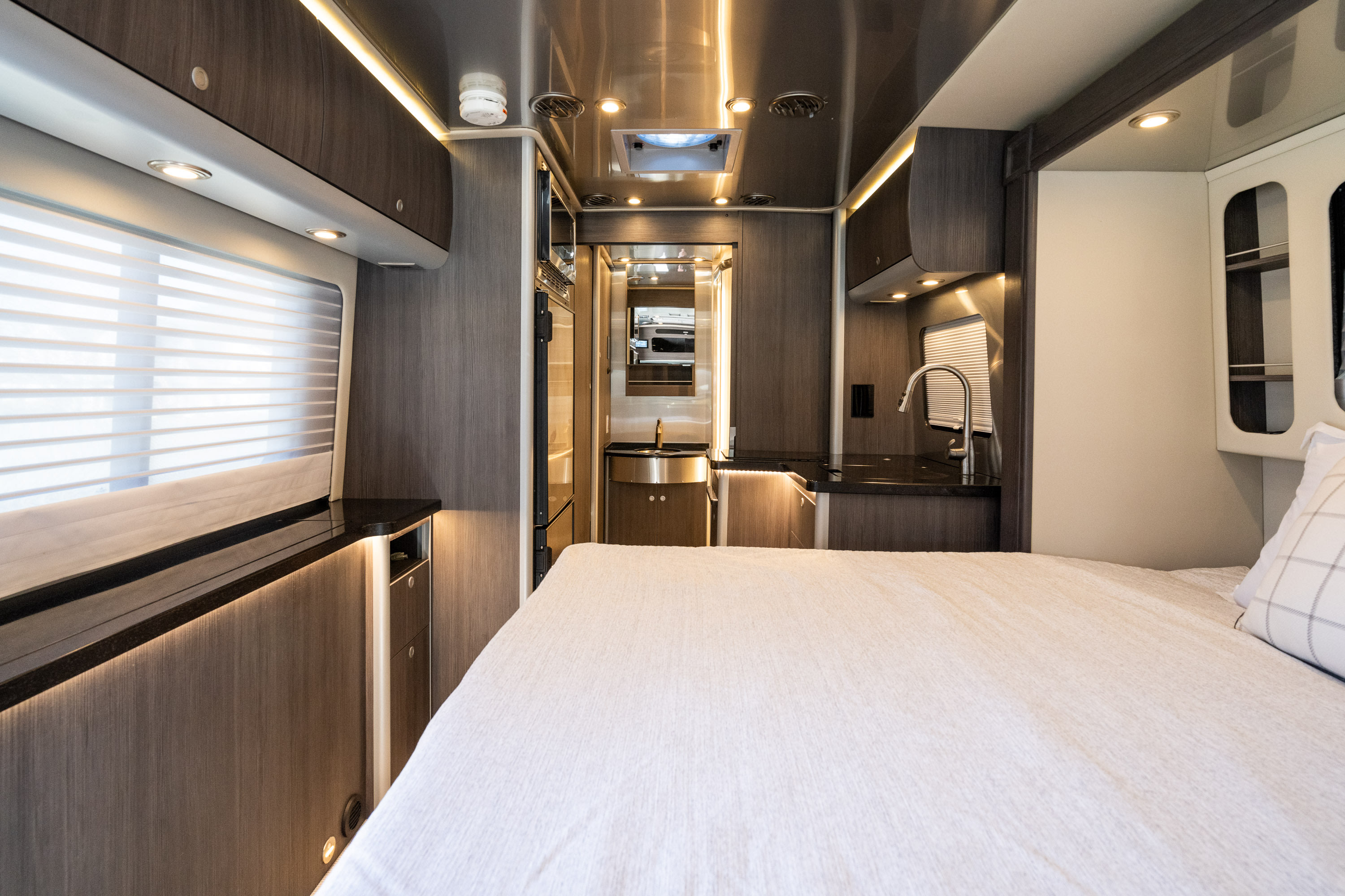 Step into a modern RV rental featuring a cozy bed, a compact kitchenette, and bright interior lighting.. Airstream Atlas 2023