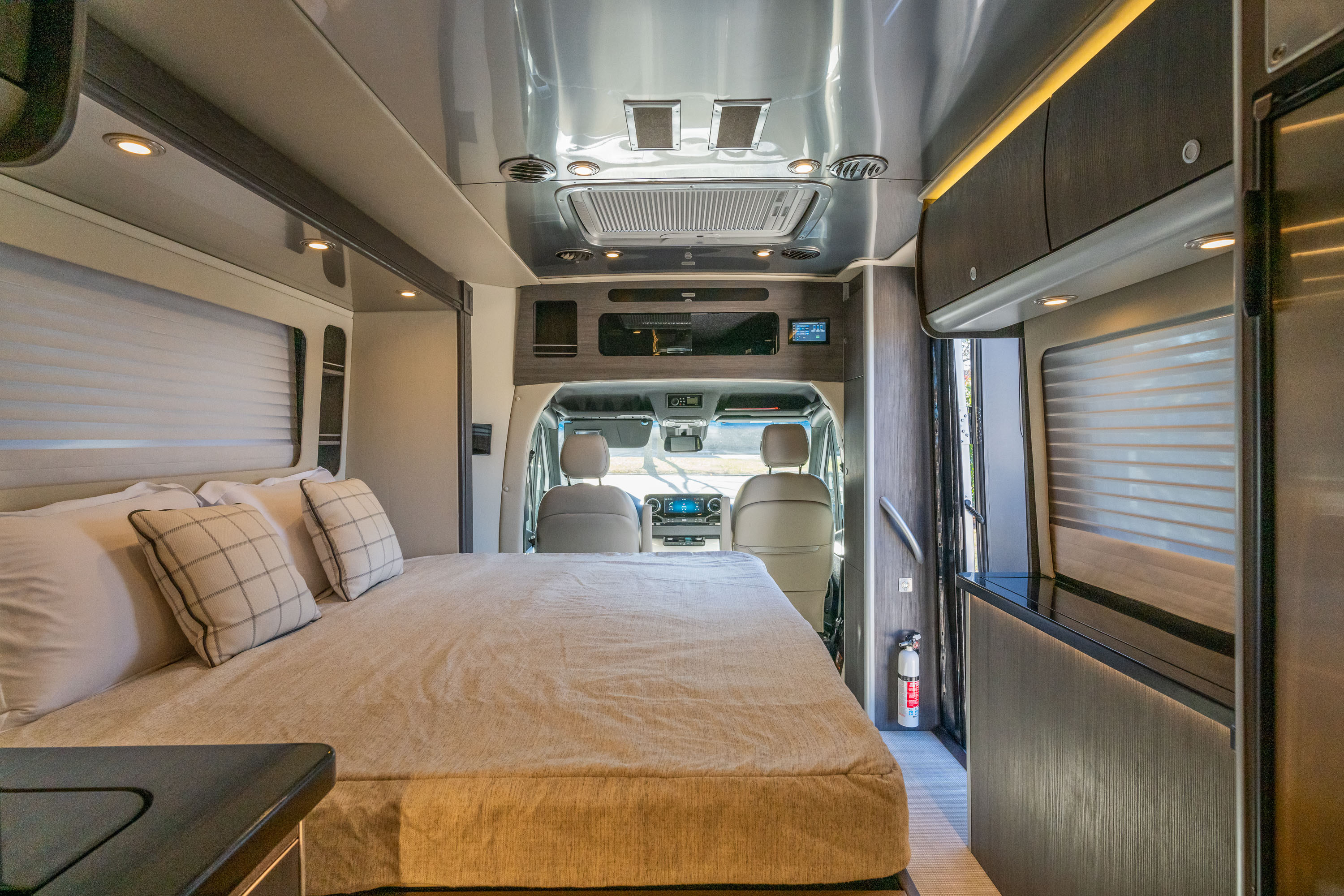 Inside a cozy RV rental: a plush bed in the foreground, with the cockpit and front seats visible beyond.. Airstream Atlas 2023