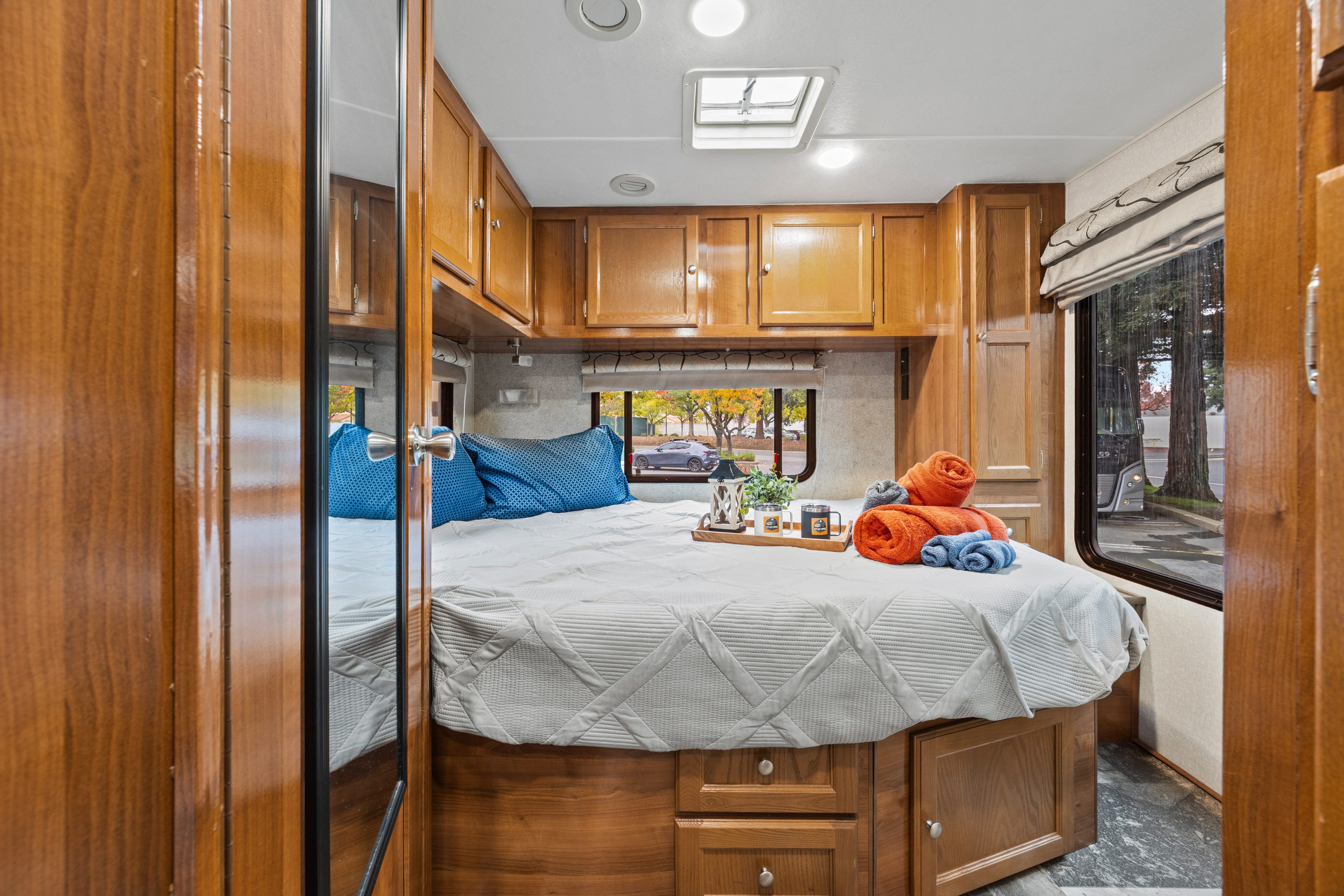 Cozy RV rental bedroom with a comfortable bed, overhead cabinets, and natural light from windows and a skylight.. Coachmen Leprechaun 2019