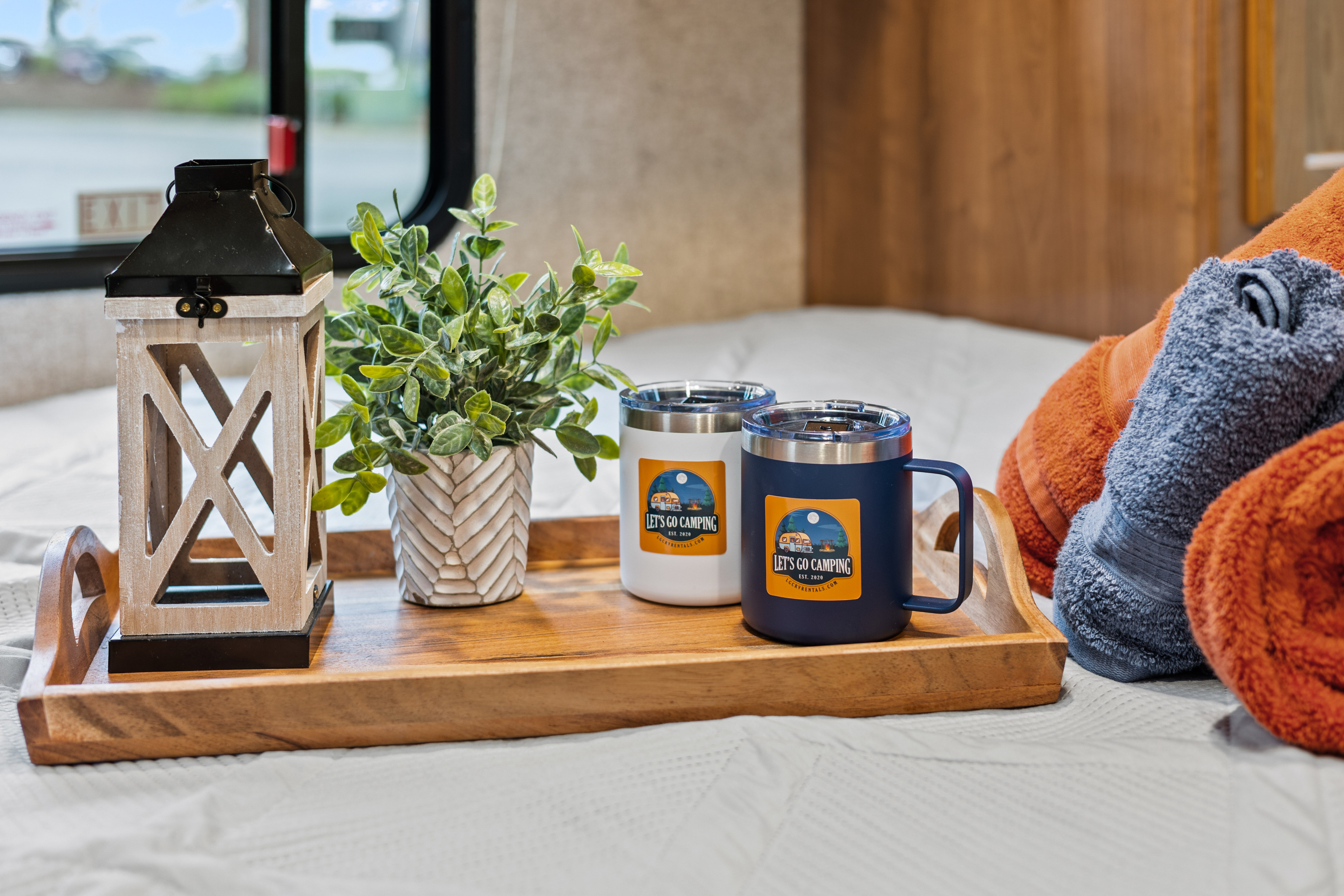 Cozy RV rental interior with "Let's Go Camping" mugs, decorative lantern, plant, and towels on a wooden tray.. Coachmen Leprechaun 2019