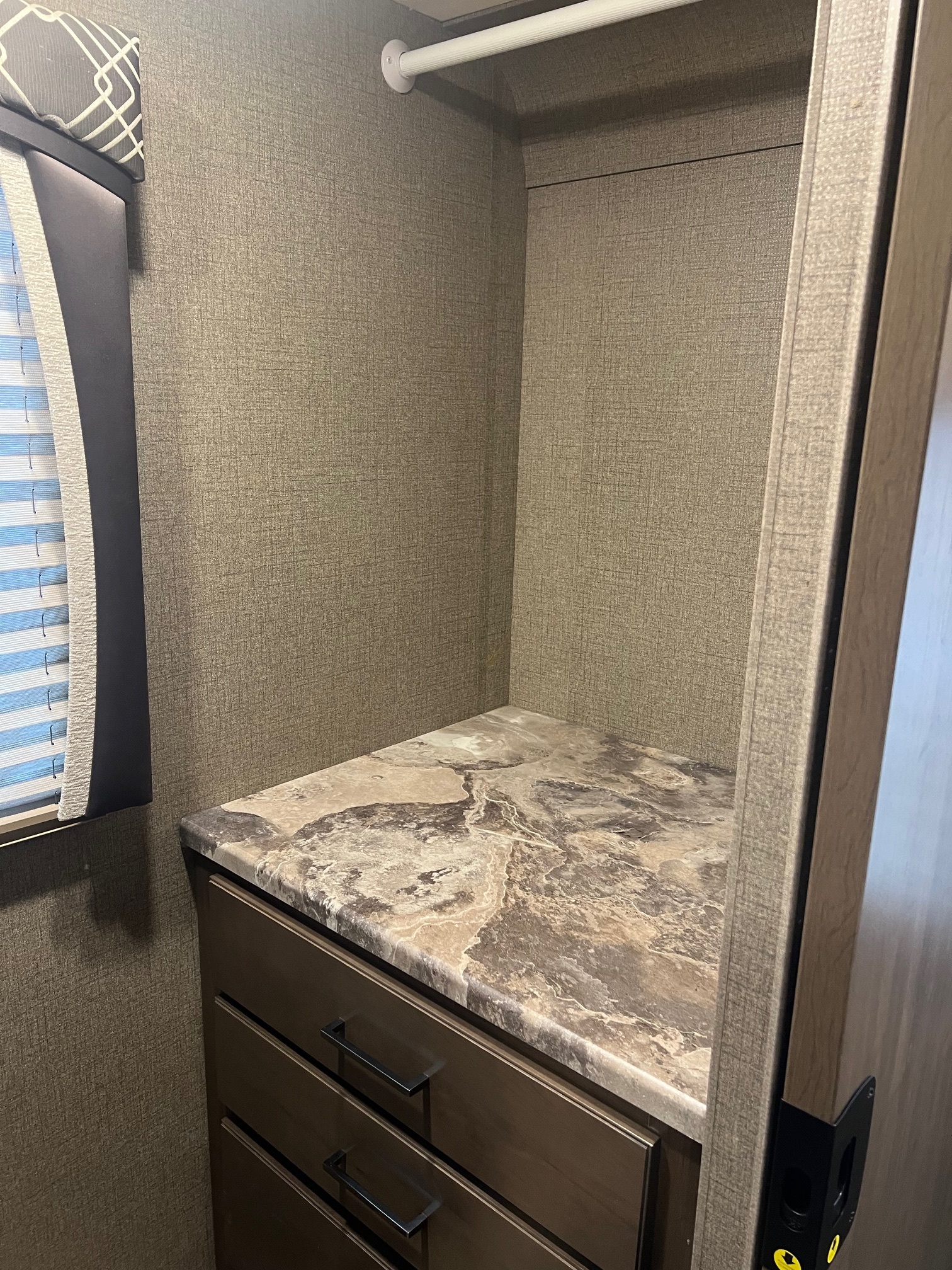 Inside an RV rental: a compact closet with a hanging rod, faux marble countertop, and drawers for storage.. Thor Chateau 2021