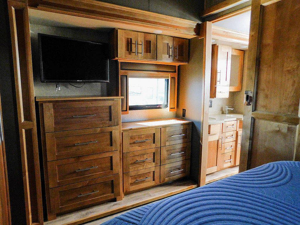 Spacious RV rental bedroom with a TV, rich wooden storage dressers, and an adjacent bathroom area.. Vanleigh RV Vilano 2018