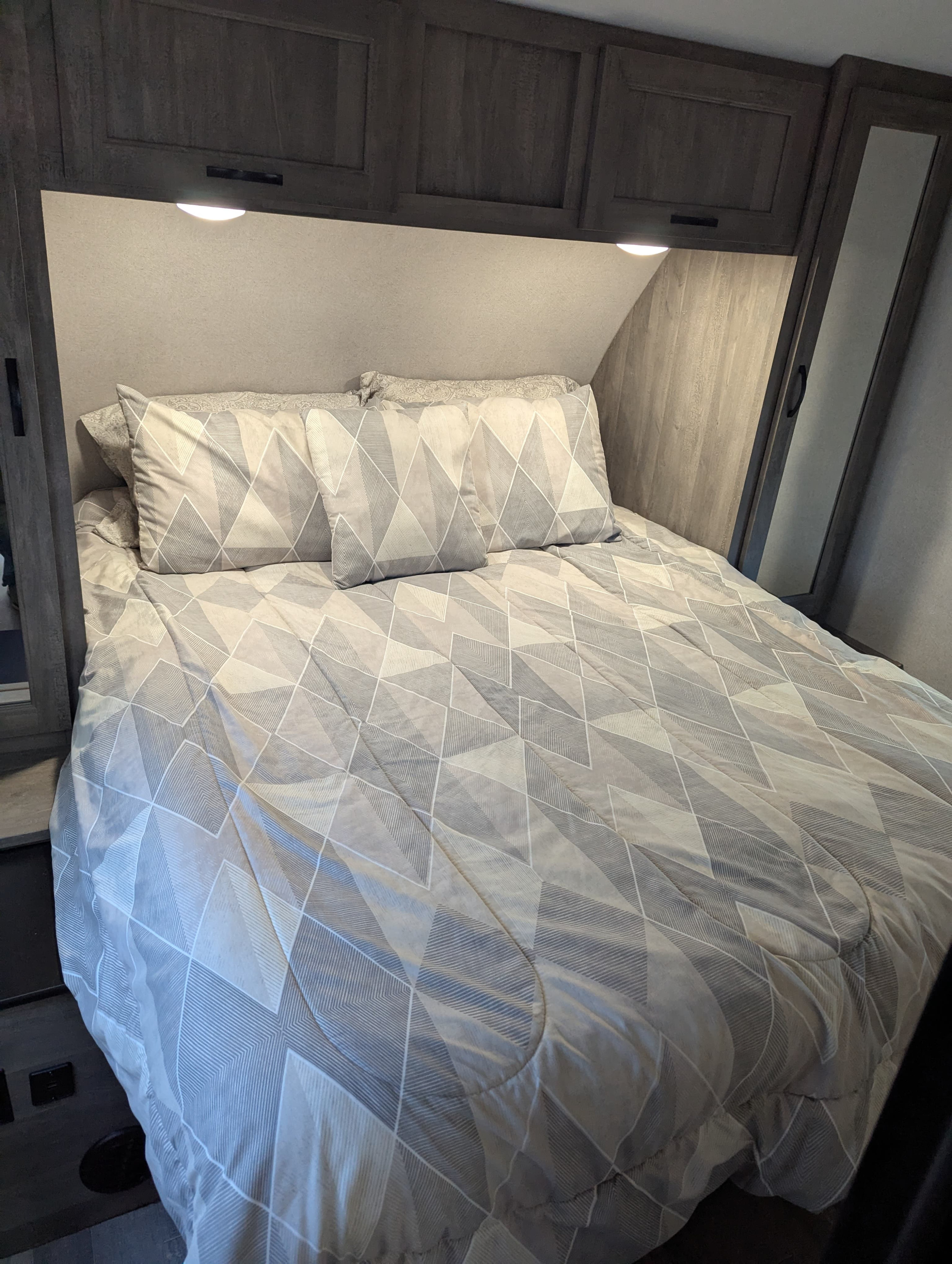 Cozy RV rental bedroom features a comfy bed with modern geometric bedding, overhead storage, and integrated lighting.. Forest River Vibe 2020