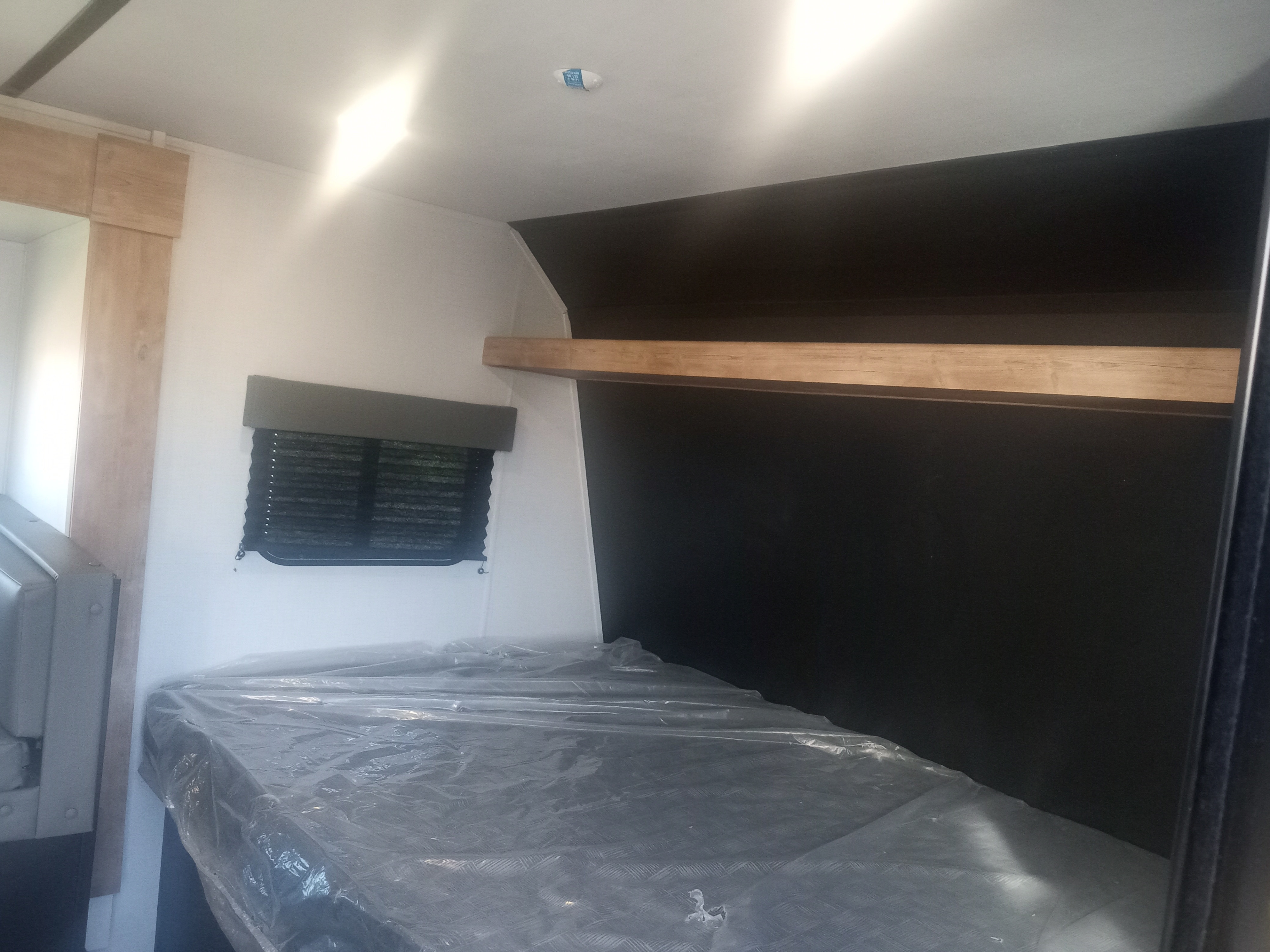 RV rental bunk bed with plastic-covered mattress and window, ready for a new journey.. Keystone RV Springdale 2023