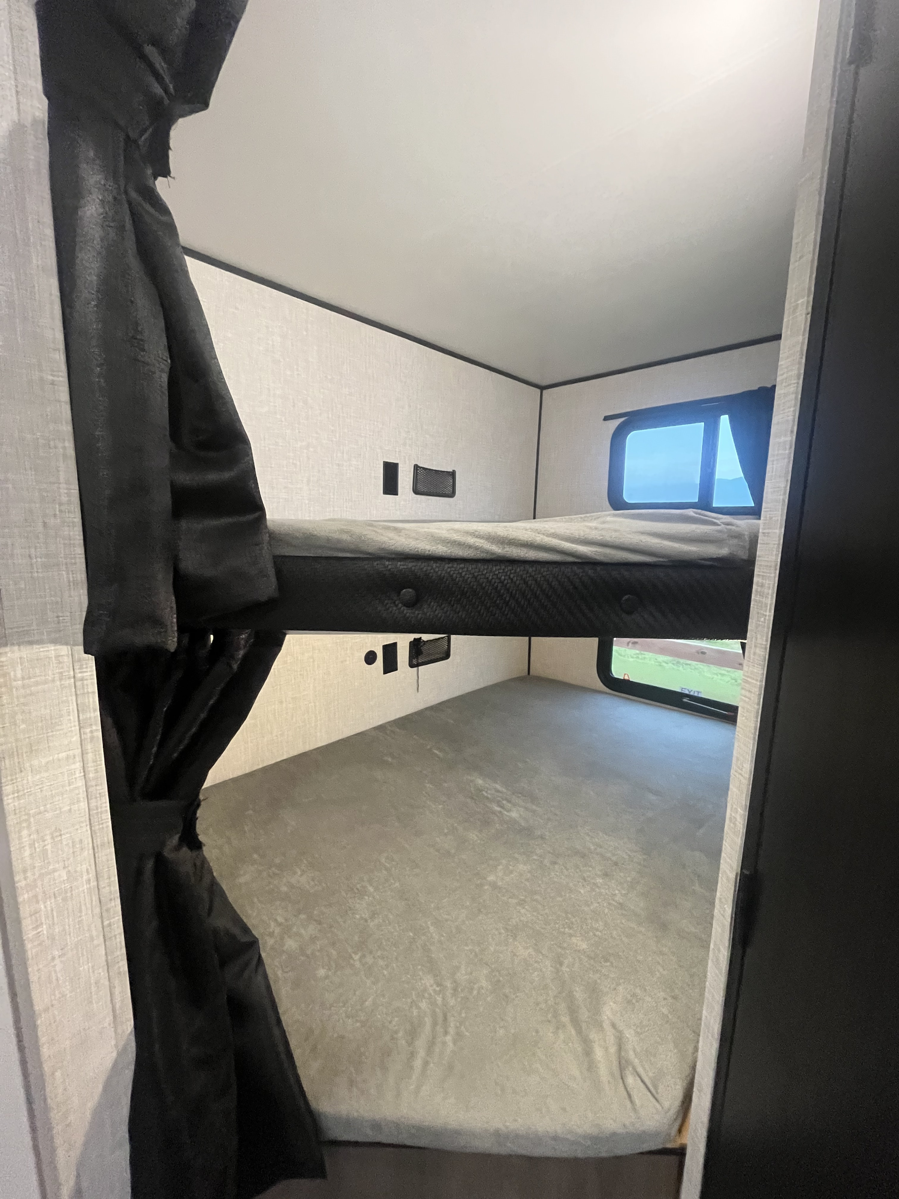 Comfortable RV rental bunk beds featuring privacy curtains, a window view, and convenient charging ports for your camper trip.. Highland Ridge RV Open Range 2025