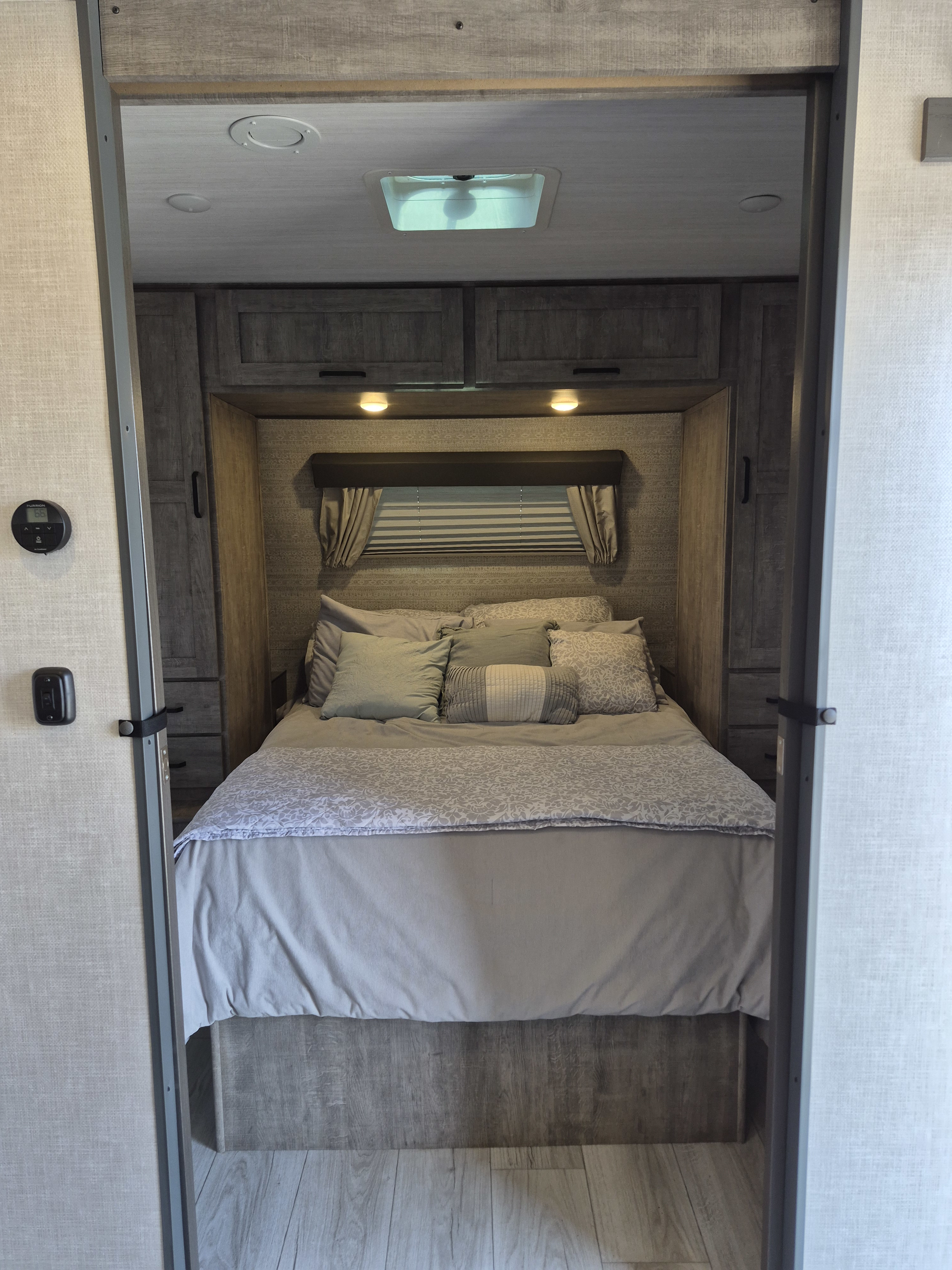 Cozy RV rental bedroom with modern decor, comfy bed, and overhead storage. Ideal for travel accommodations.. Forest River Surveyor Legend 2023