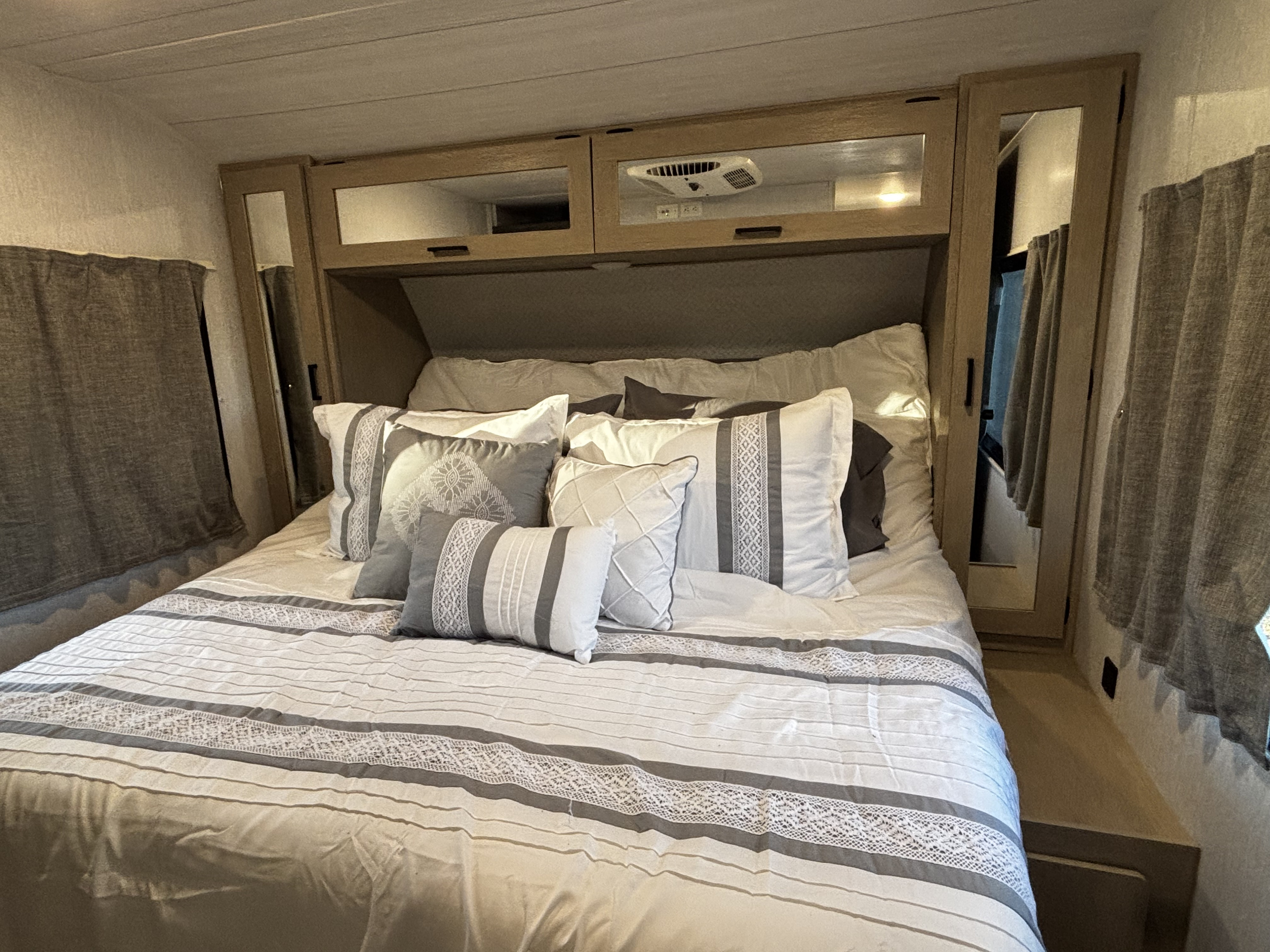 Cozy RV rental bedroom featuring a neatly made bed with white & gray pillows, and overhead storage.. Forest River Wildwood Heritage Glen 2024