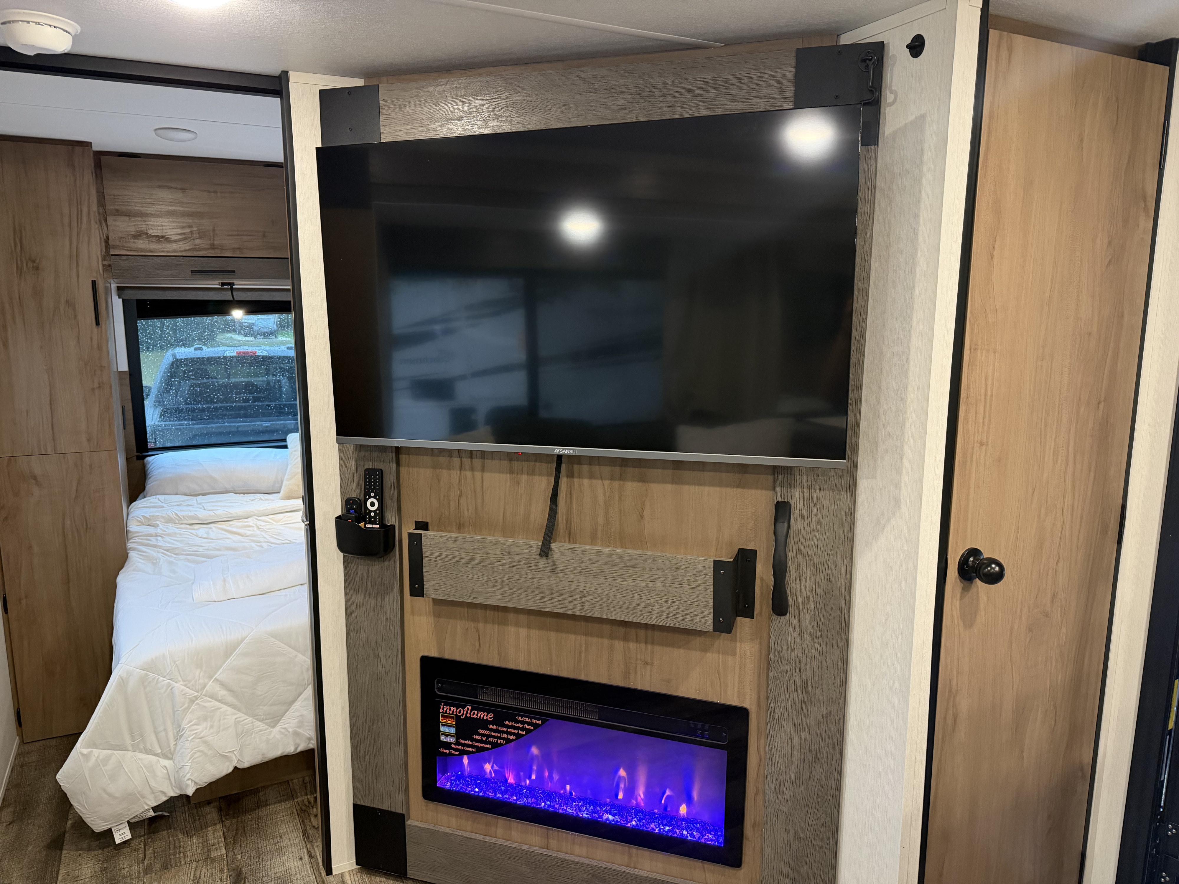Modern RV rental interior featuring a SANSUI TV above an innoflame electric fireplace, with a cozy bedroom visible beyond.. Forest River Campsite Reserve 2025