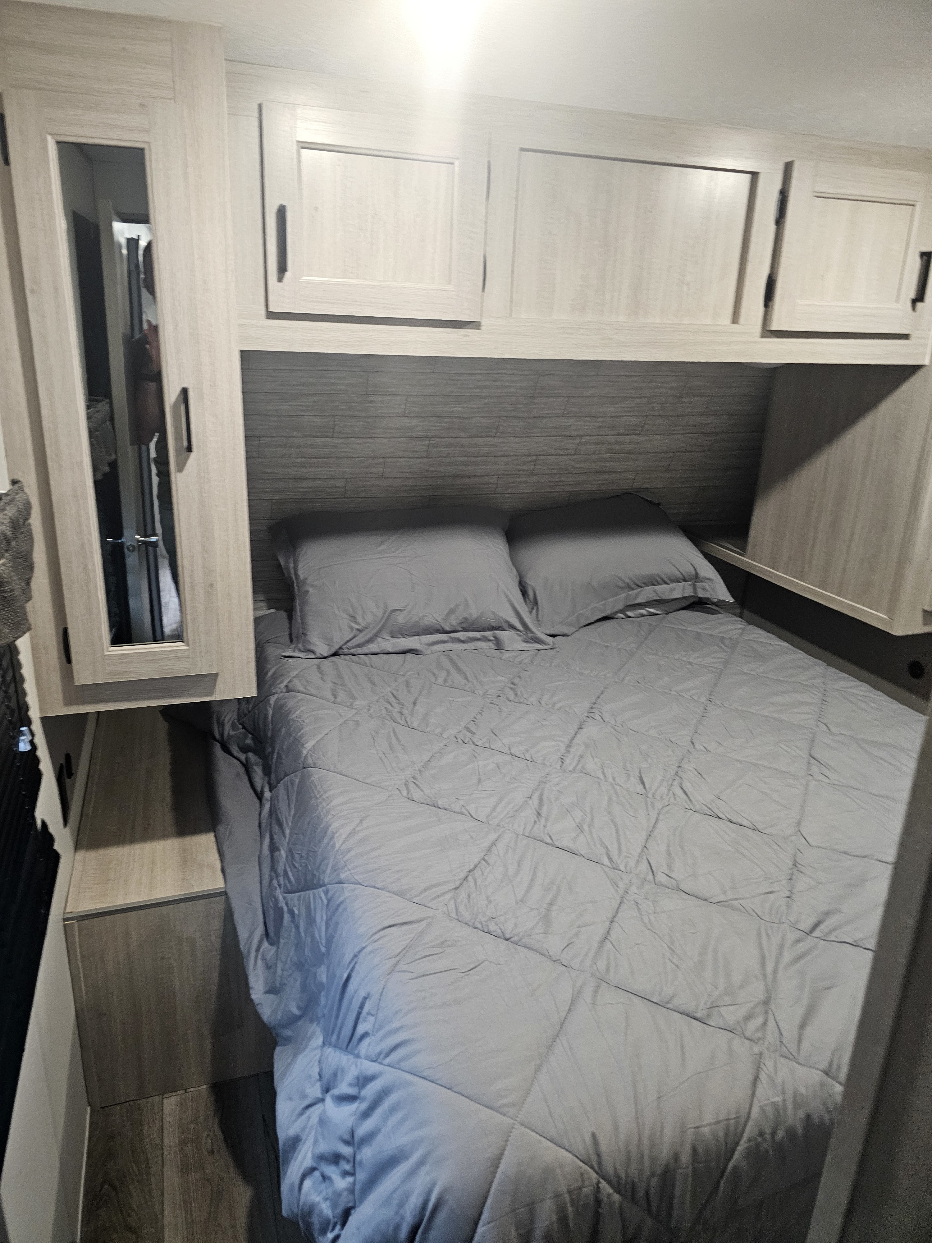 Cozy RV rental bedroom with a bed, gray bedding, overhead cabinets, and a mirrored wardrobe.. Coachmen Catalina legacy edition 293TQBSCK 2025