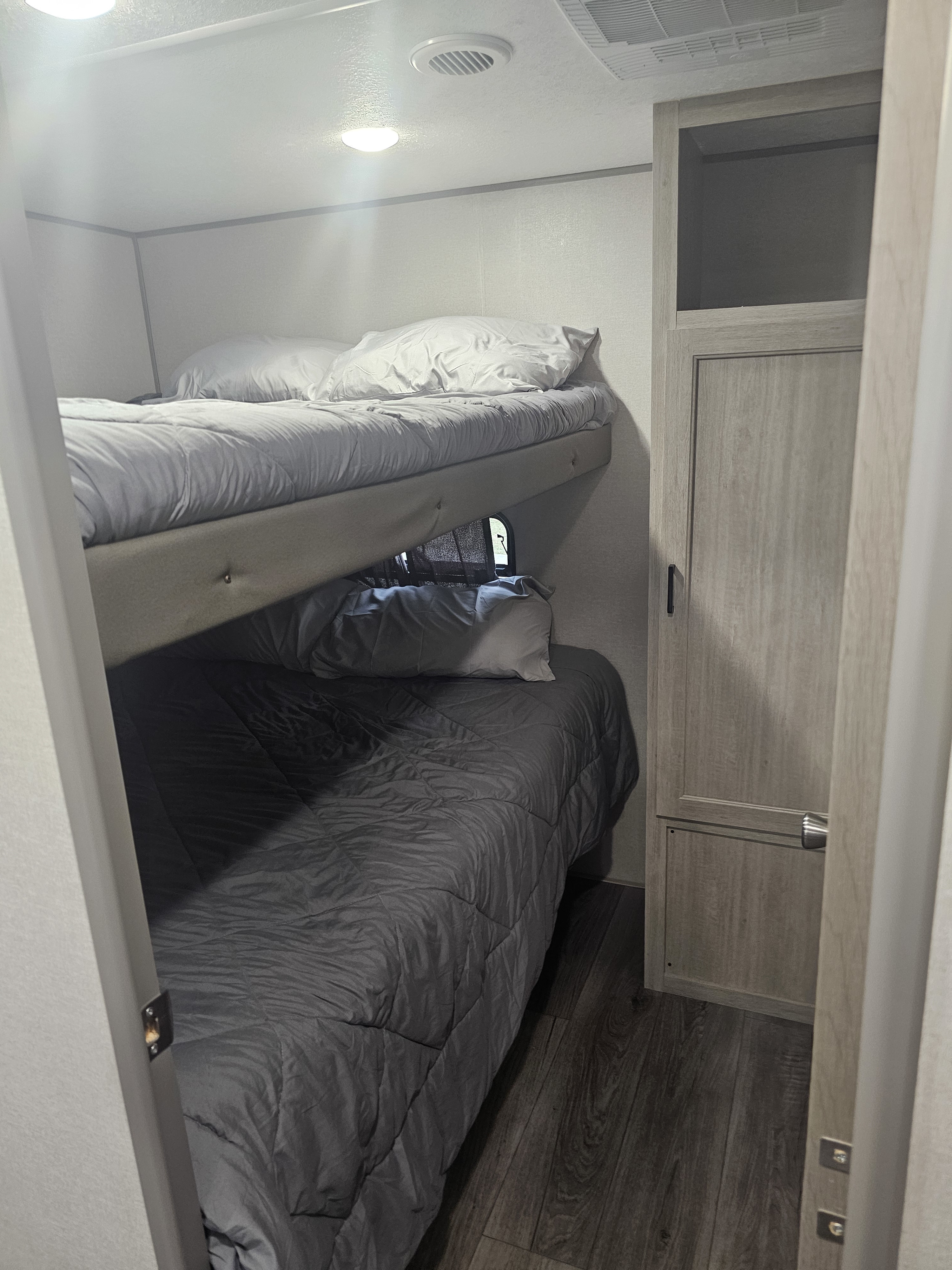 RV rental interior: two stacked bunk beds with grey bedding and a light wood wardrobe, providing a compact sleeping area.. Coachmen Catalina legacy edition 293TQBSCK 2025