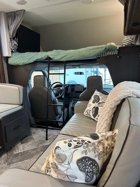 Spacious rv rental interior showing an over-cab bunk bed, living area with sofa, and dining bench on the left.. Forest River Sunseeker 2022