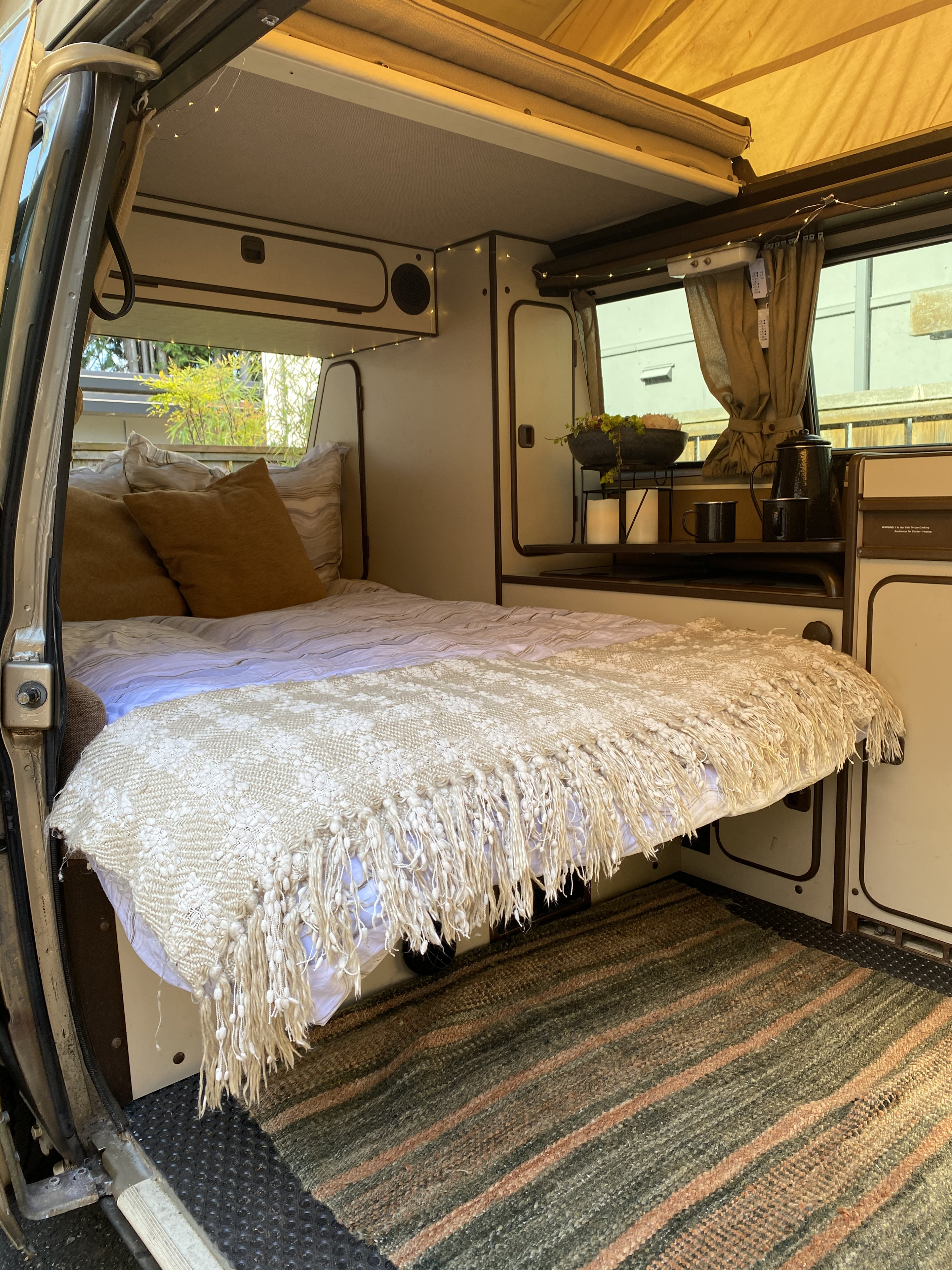 This RV rental offers a cozy campervan interior with a comfortable bed, mini kitchen setup, and soft lighting for travel.. Volkswagen T3 Westfalia 1985