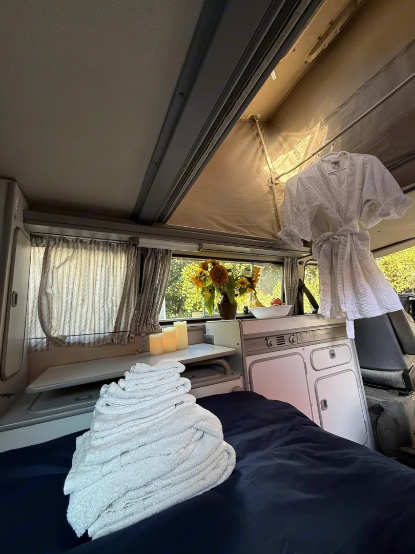 This cozy RV rental features a comfy bed, compact kitchen, and pop-top roof. Towels and bathrobe ready for your camper adventure!. Volkswagen Westfalia 1986