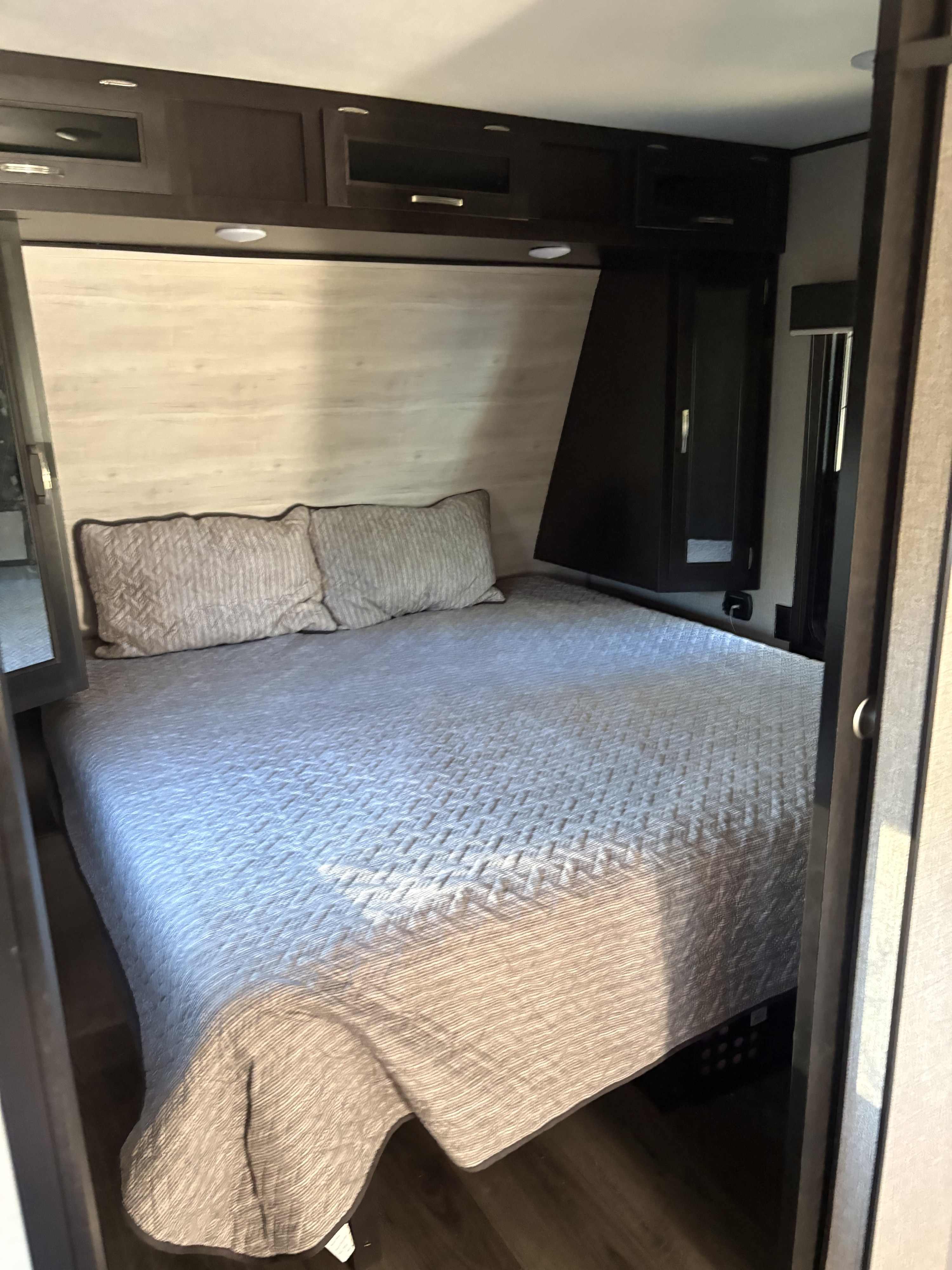 Cozy RV rental bedroom featuring a queen bed with pillows, wood paneling, and overhead storage cabinets.. Jayco Jay Flight 2021