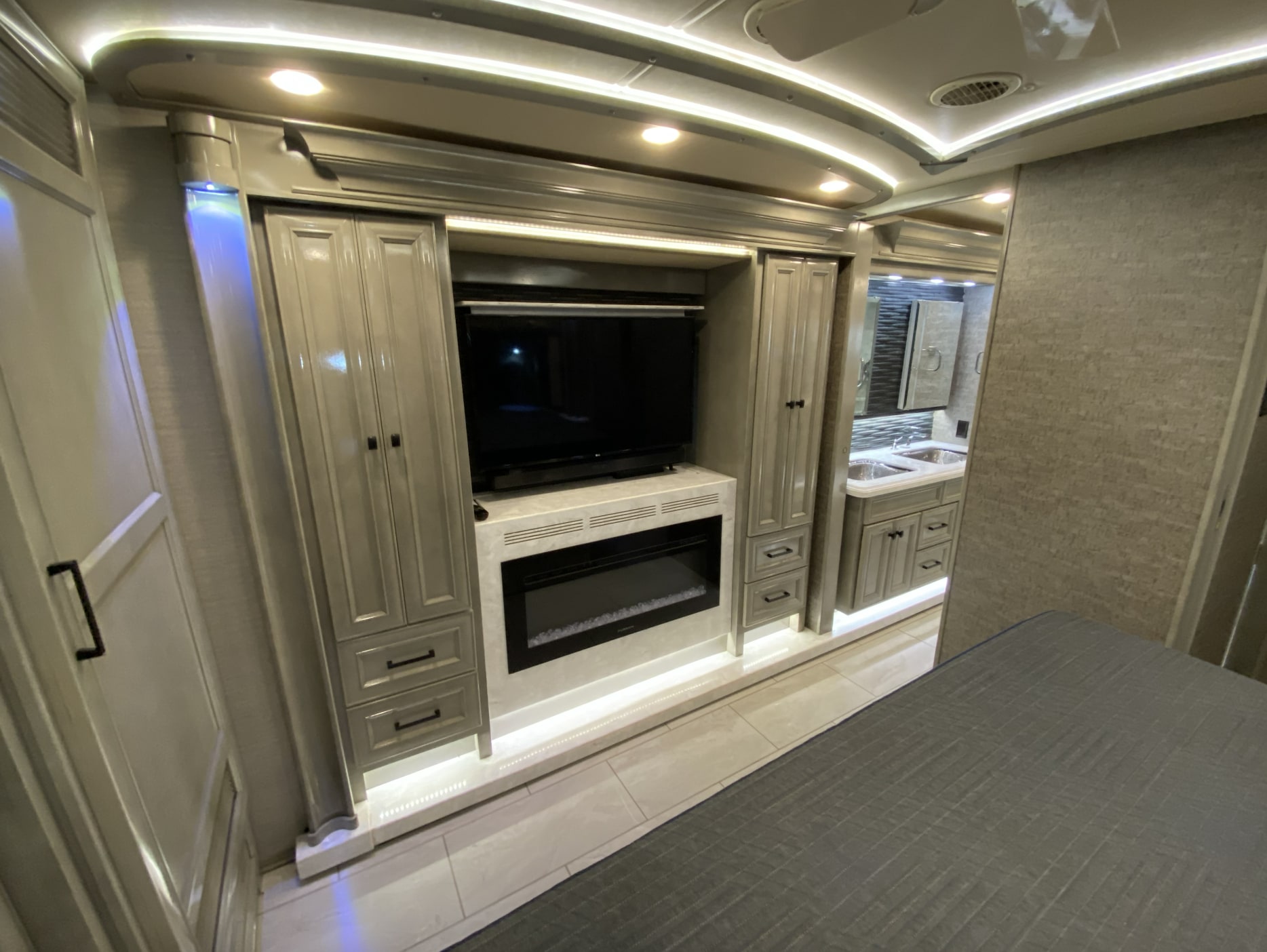Spacious RV rental bedroom with TV, electric fireplace, sleek cabinetry, and integrated bathroom vanity area.. Tiffin Bus 2020