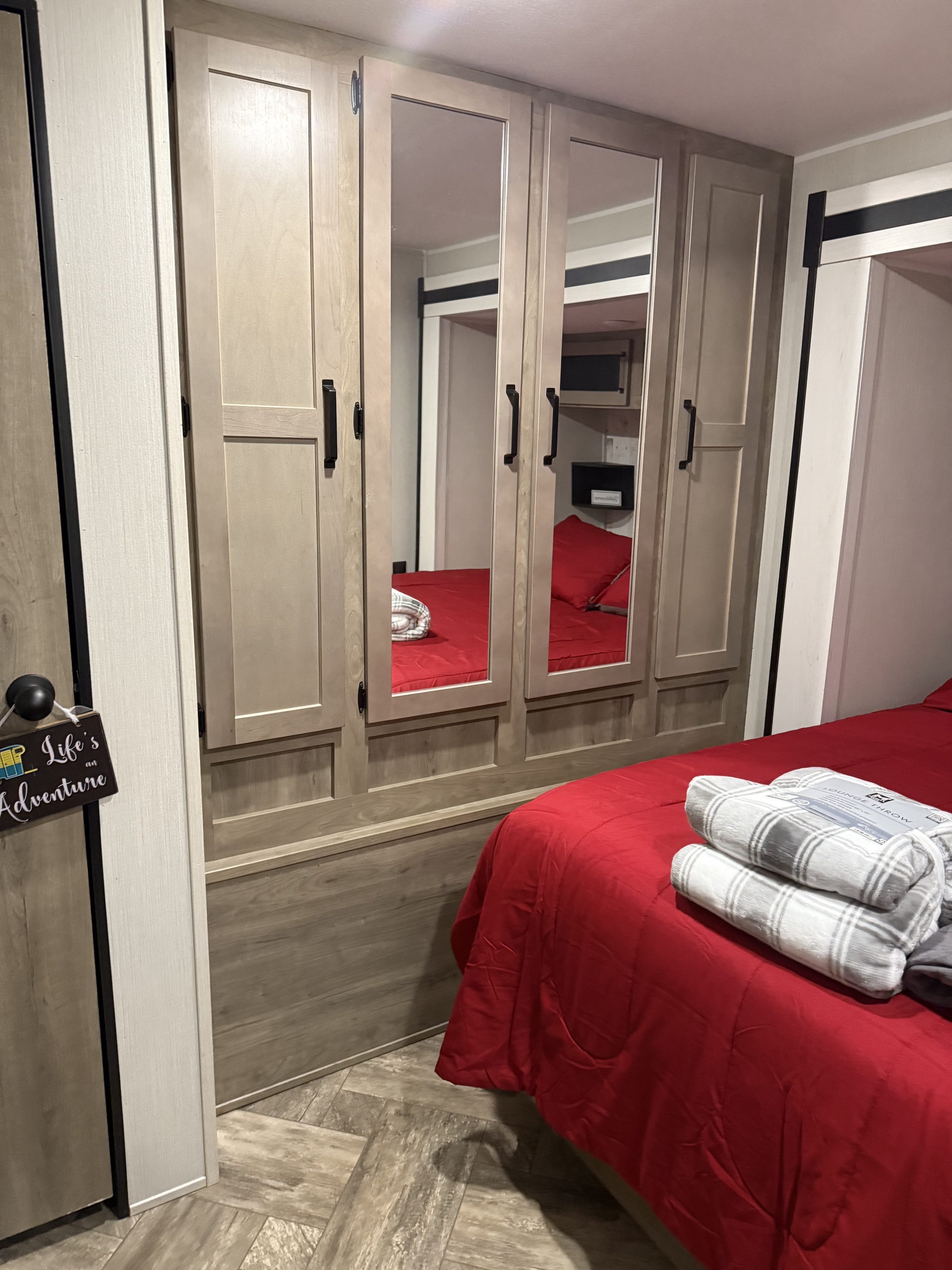 RV rental bedroom showing a red bed, mirrored closet, and "Life's an Adventure" sign on a door.. Forest River Palomino Puma 2023