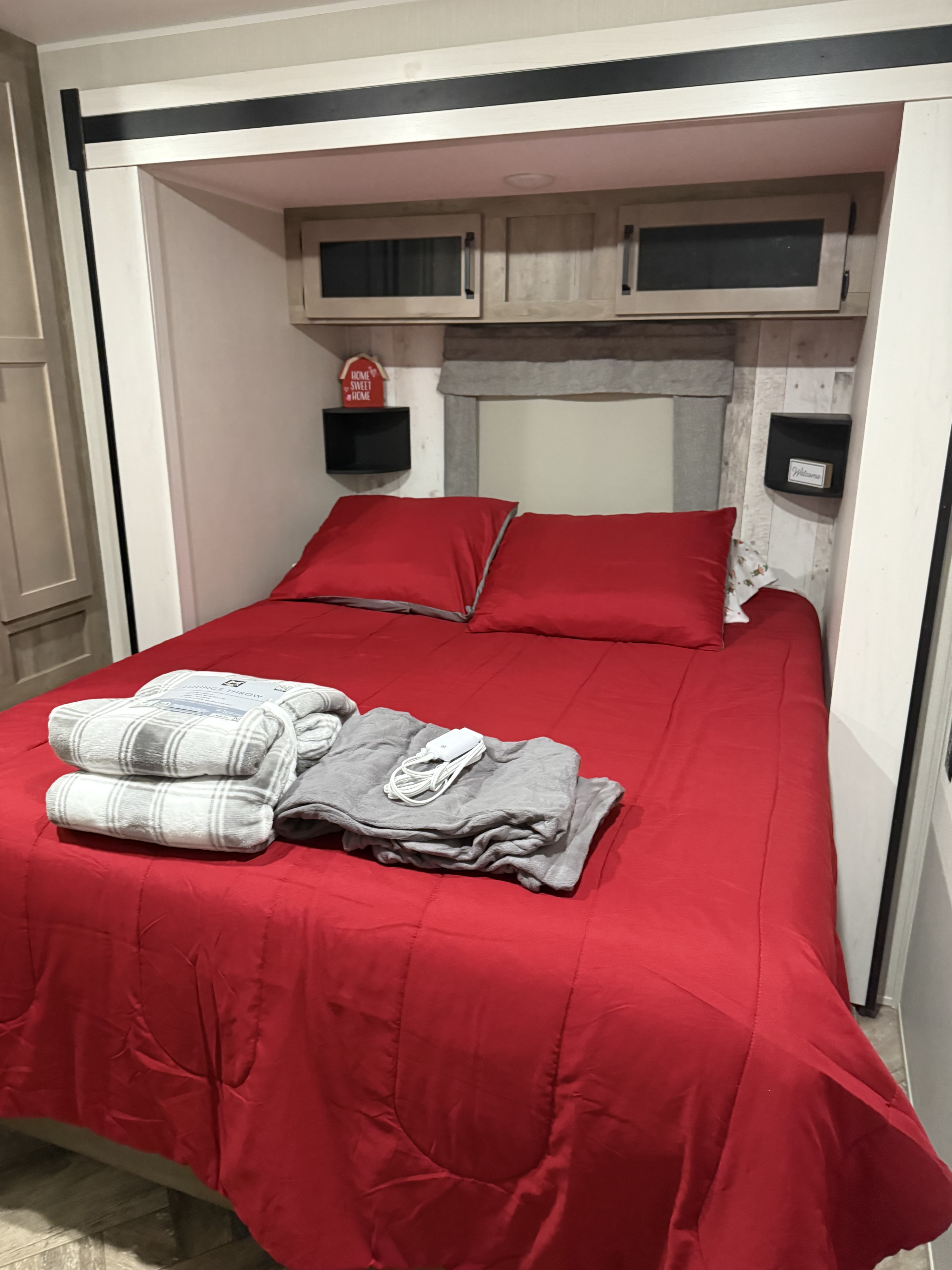 Cozy RV rental bedroom with a vibrant red bed, pillows, plaid and gray blankets, plus convenient overhead storage.. Forest River Palomino Puma 2023
