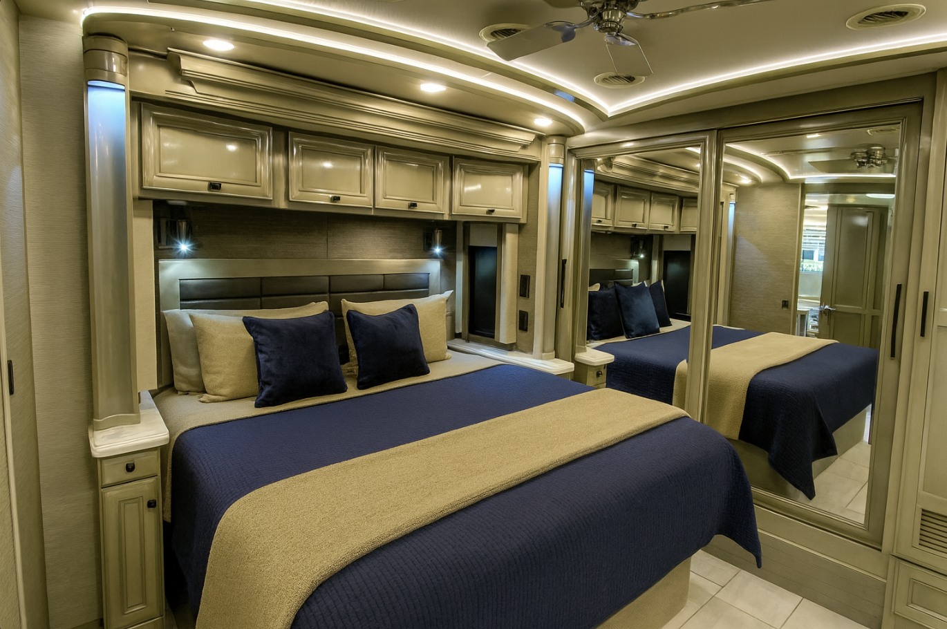 Experience comfort in this RV rental bedroom: large bed with navy bedding, overhead storage, and mirrored wardrobe.. Tiffin Bus 2020