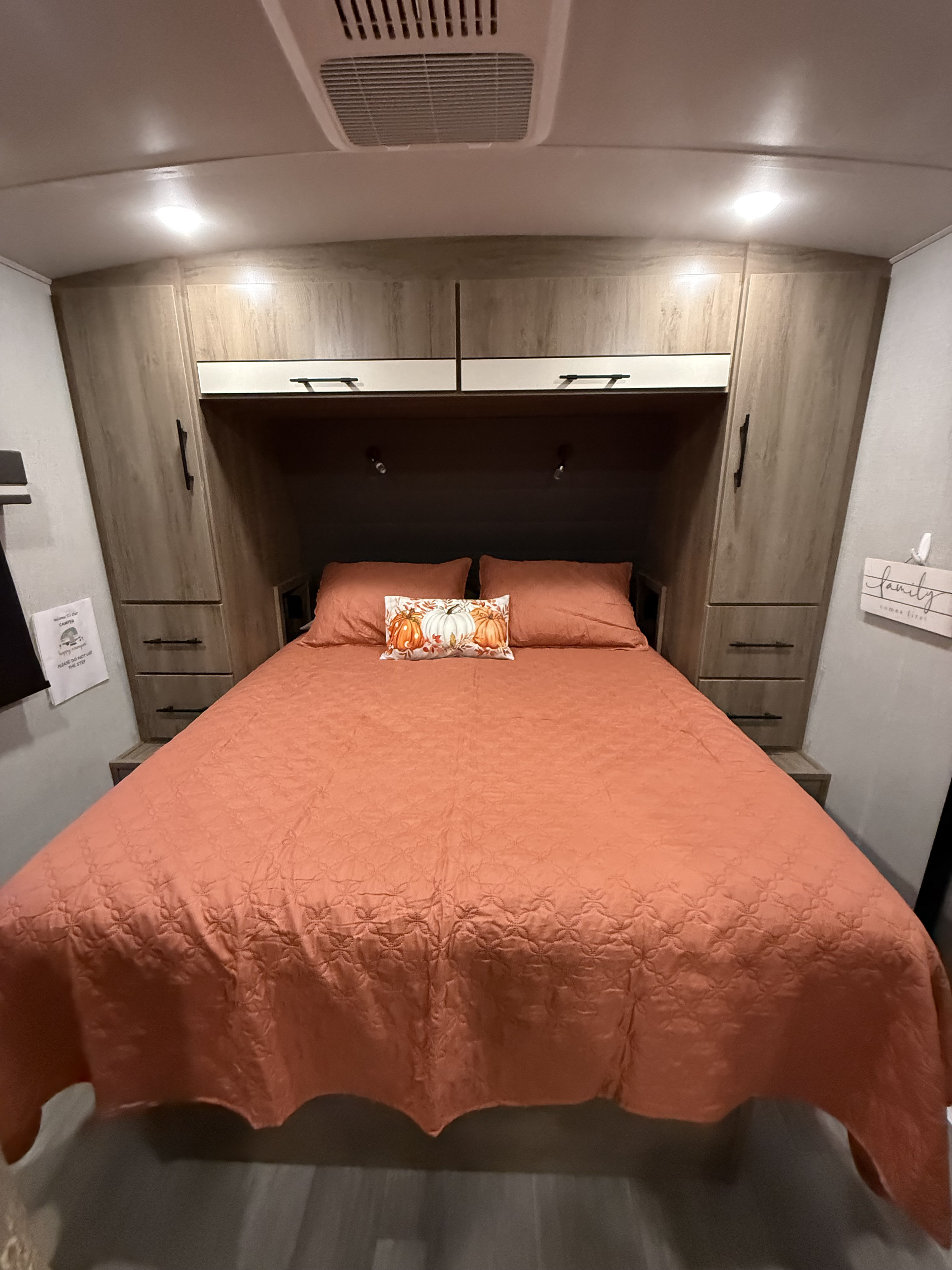 Cozy fall-themed RV rental bedroom featuring an orange bed, pumpkin pillow, and ample storage for a comfortable camper stay.. Grand Design Imagine 2023