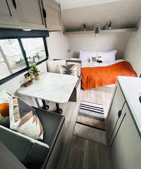 Inviting RV rental interior: cozy bed with orange blanket, dinette, & compact kitchen, ready for adventure.. Coachmen Clipper 2025