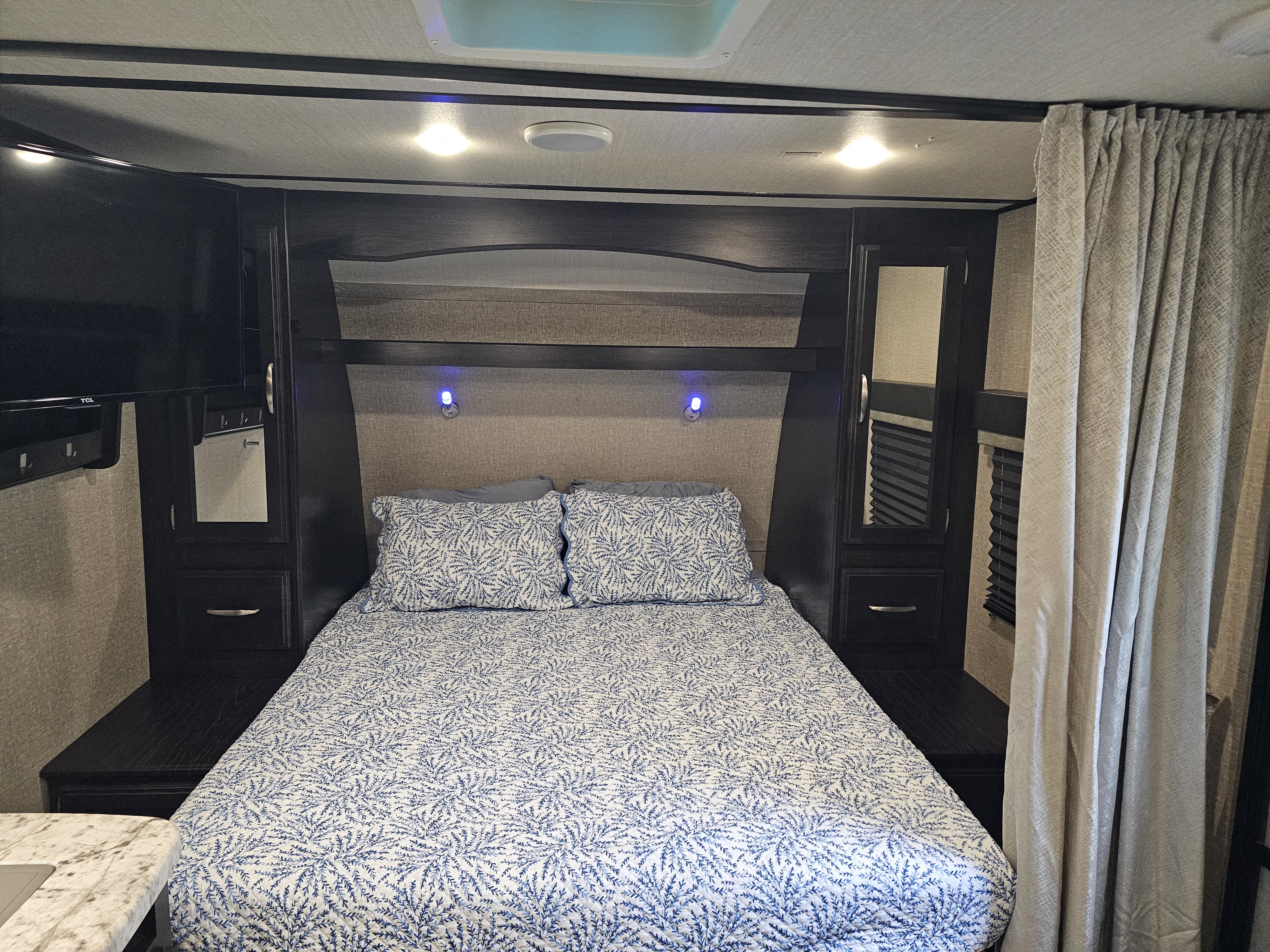 Cozy RV rental bedroom with blue and white patterned bedspread, built-in storage, and reading lights.. Grand Design Imagine XLS 2019