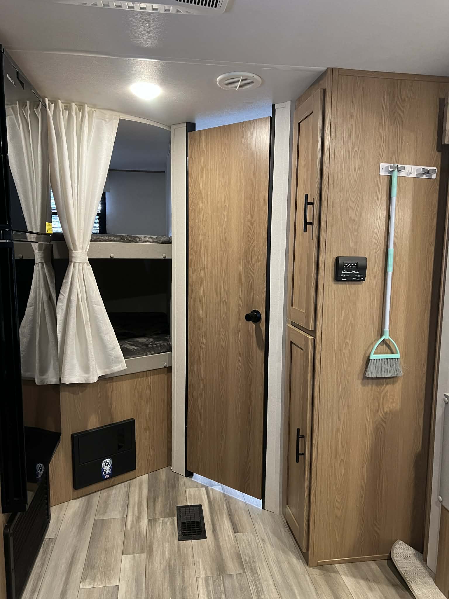 RV rental interior featuring bunk beds with privacy curtains, sleek wood cabinetry, and a mounted broom for tidy living.. AVENGER 24BHSLE 2023