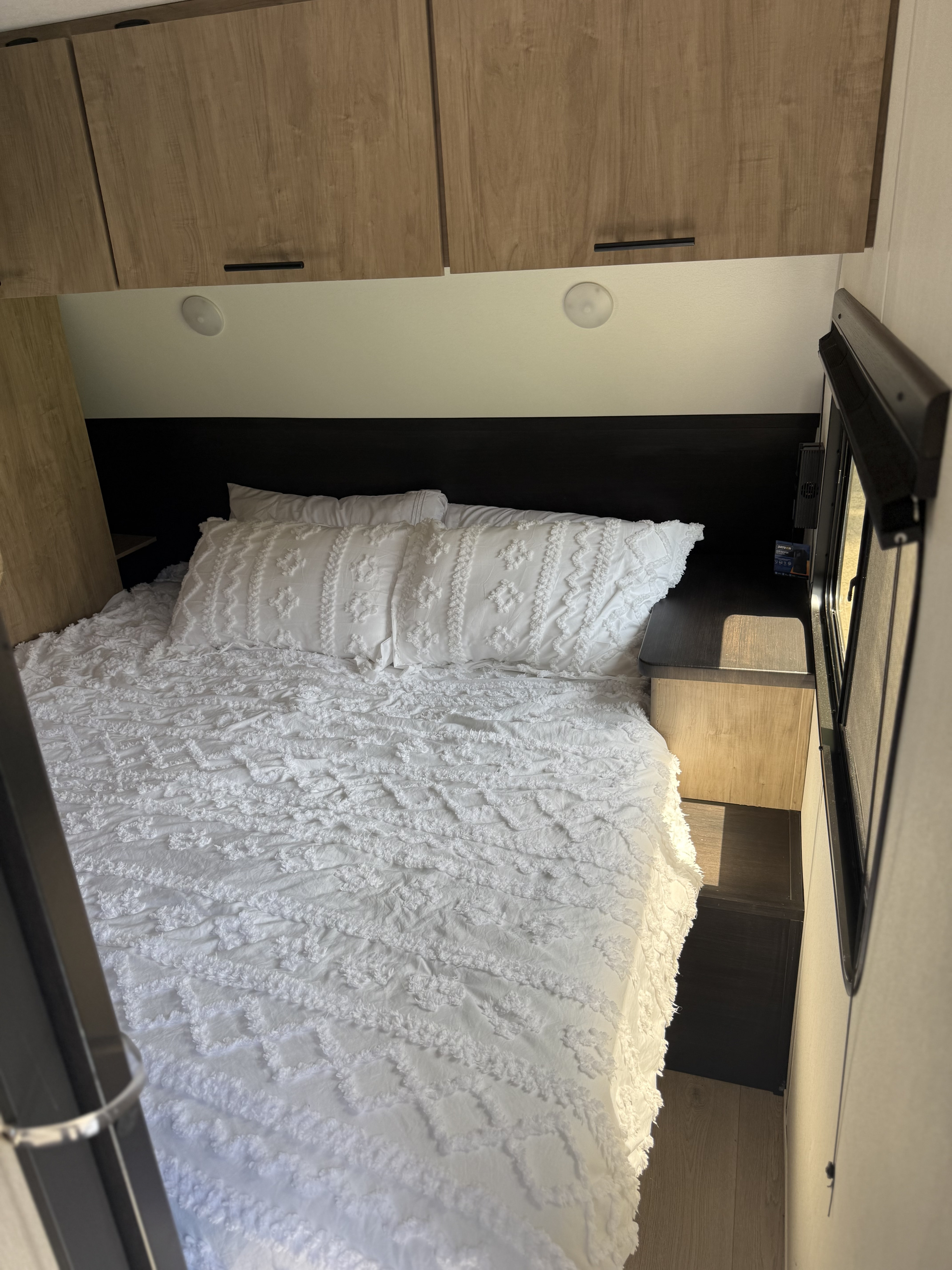 Bright rv rental bedroom with a white textured bed, dark headboard, and wood overhead cabinets. A compact and inviting sleeping space.. Forest River Cherokee Grey Wolf 2026