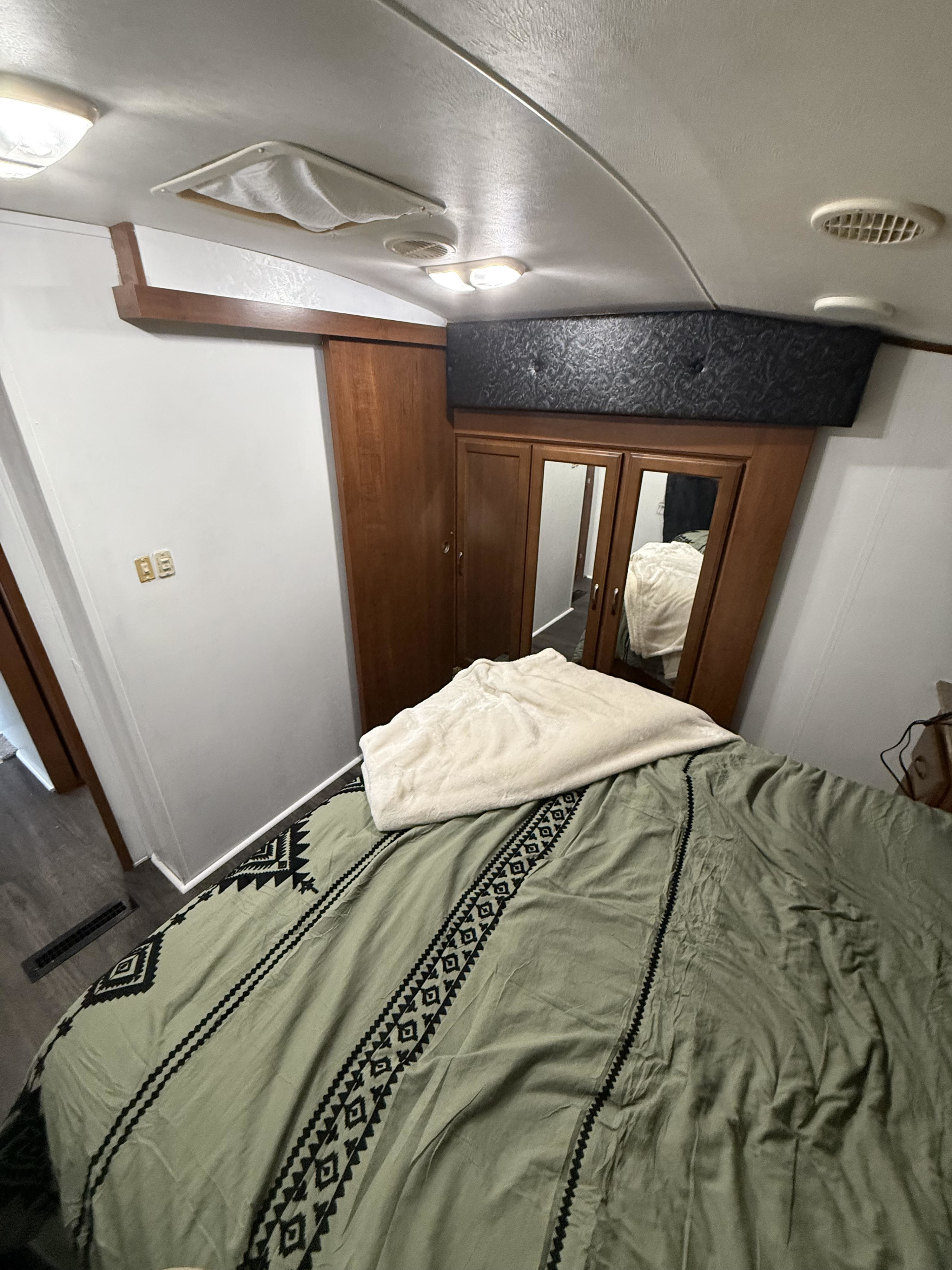 Compact RV rental bedroom: a cozy space with a patterned bed, mirrored wardrobe, and overhead lighting for your adventure.. Heartland RVs Sundance 2013