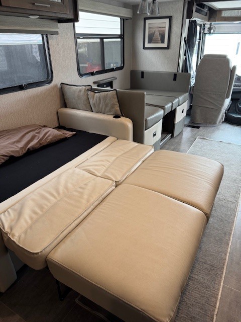 RV rental interior: A beige sofa bed is extended in a modern motorhome's living area, with a dinette beyond.. Forest River Coachmen Mirada 2023