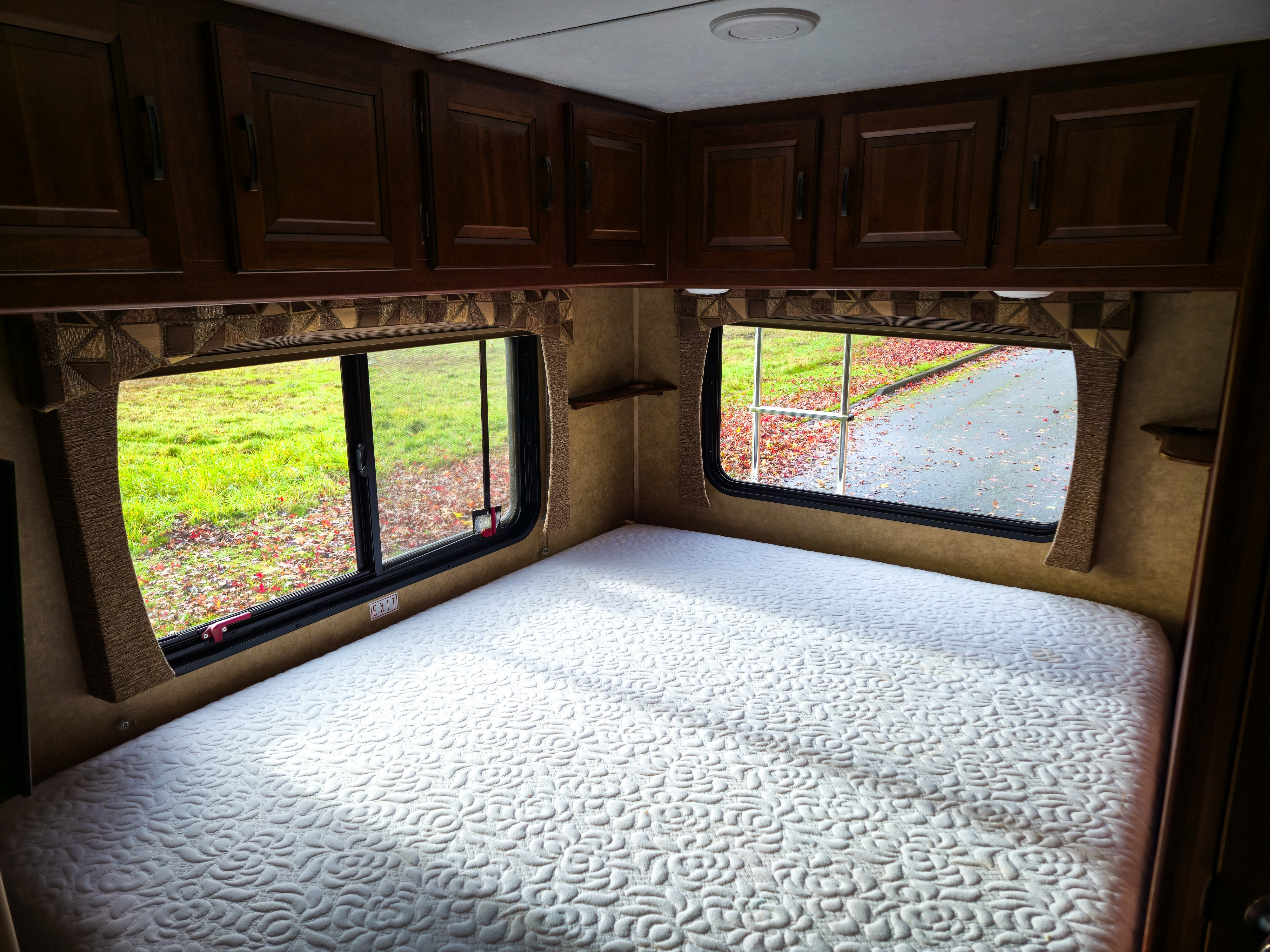 Enjoy this RV rental bedroom featuring a quilted white bed, storage cabinets, and scenic window views outside.. Forest River Sunseeker 2015