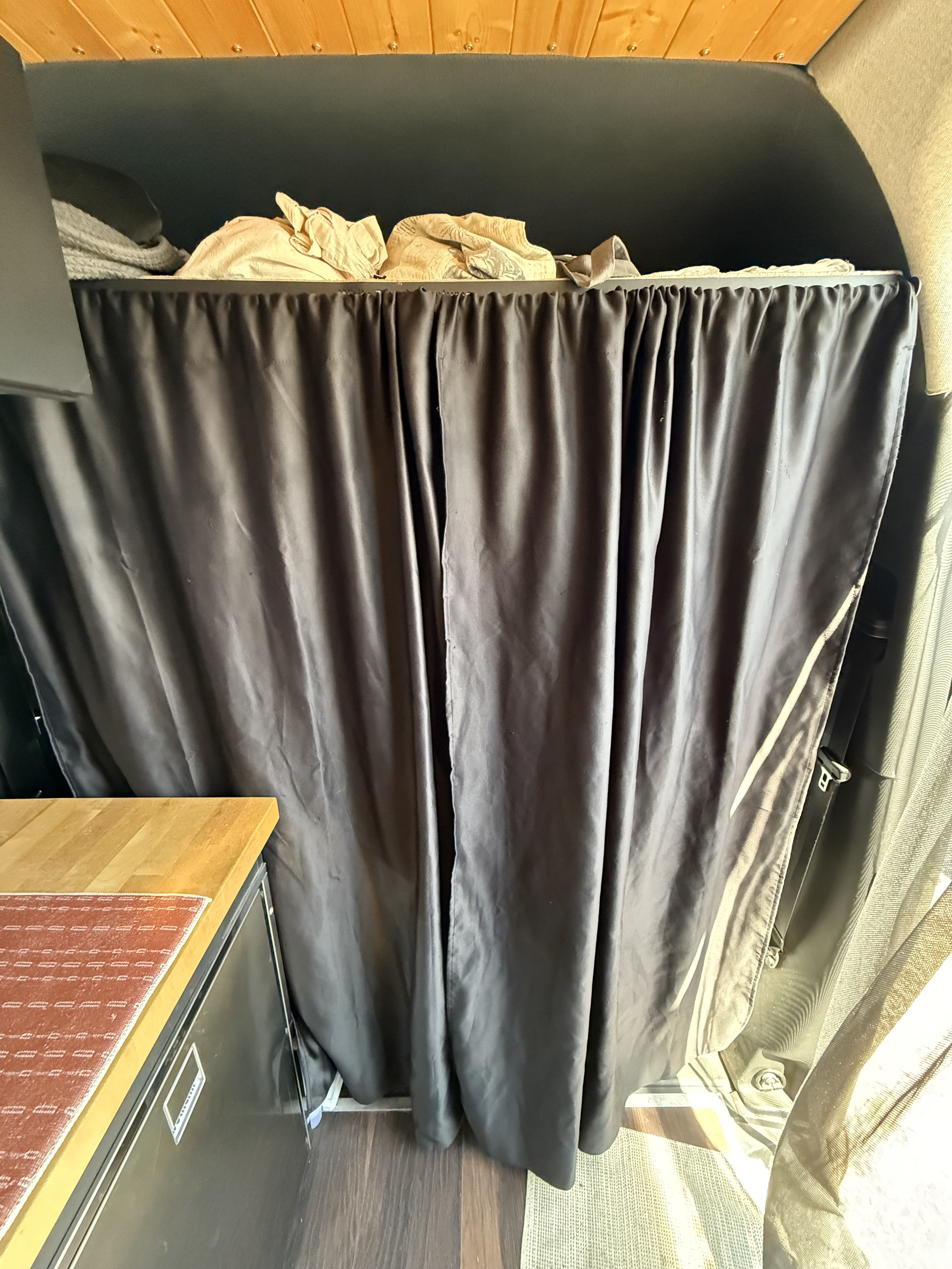 RV rental interior: organized storage behind a dark curtain, with a wood-paneled ceiling, compact counter, and integrated fridge.. Mercedes-Benz Sprinter 2019